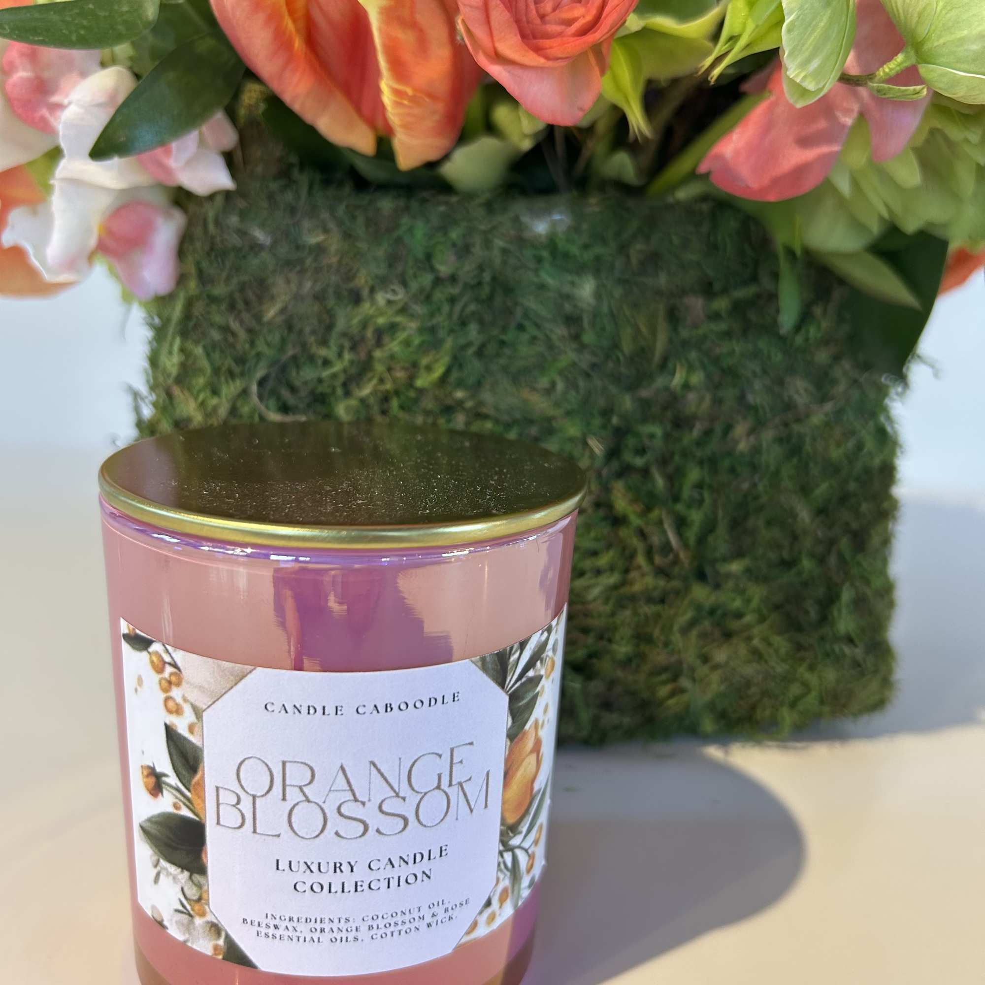 Pink-orange floral arrangement behind an orange blossom candle