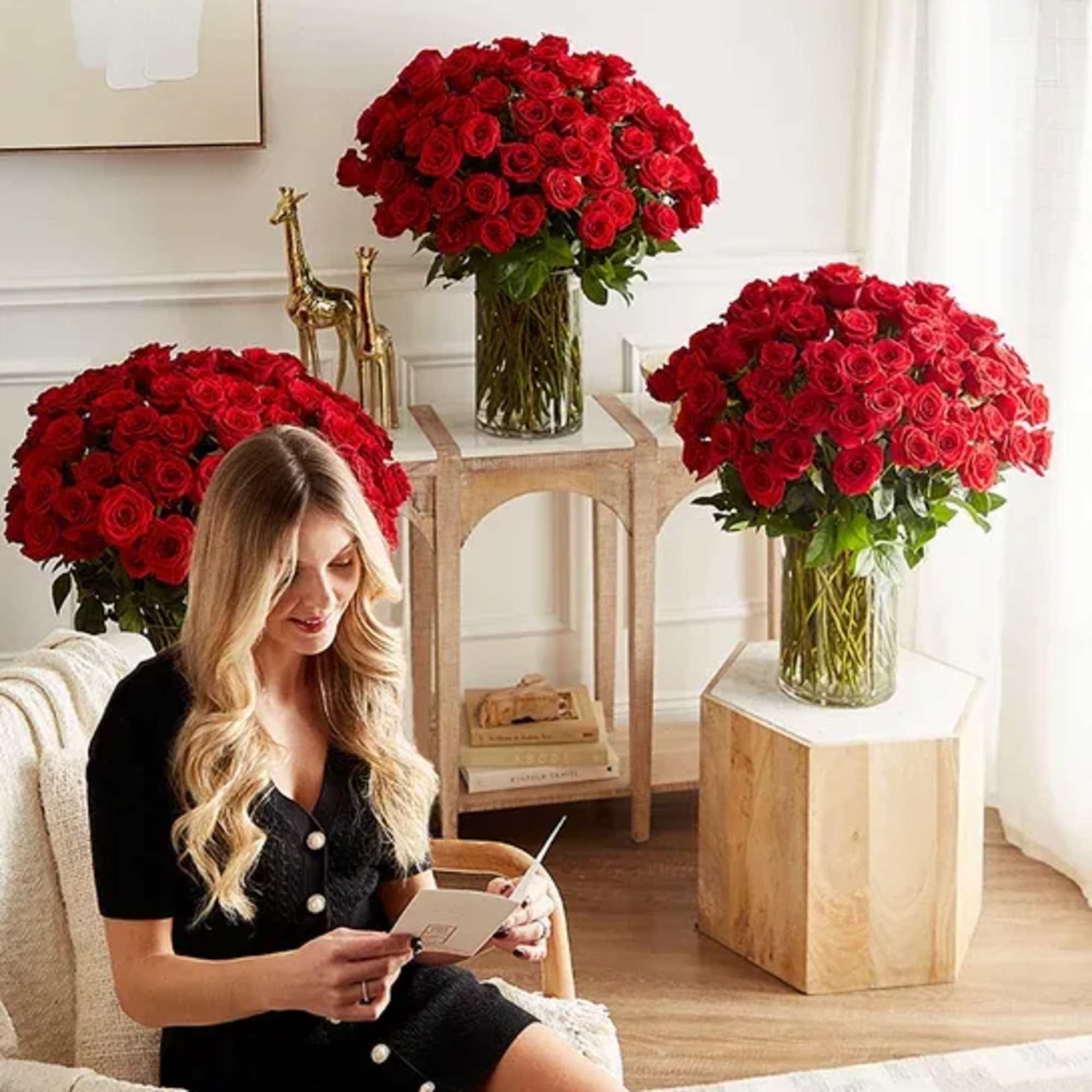 Three large red rose arrangements in glass vases in a bright room