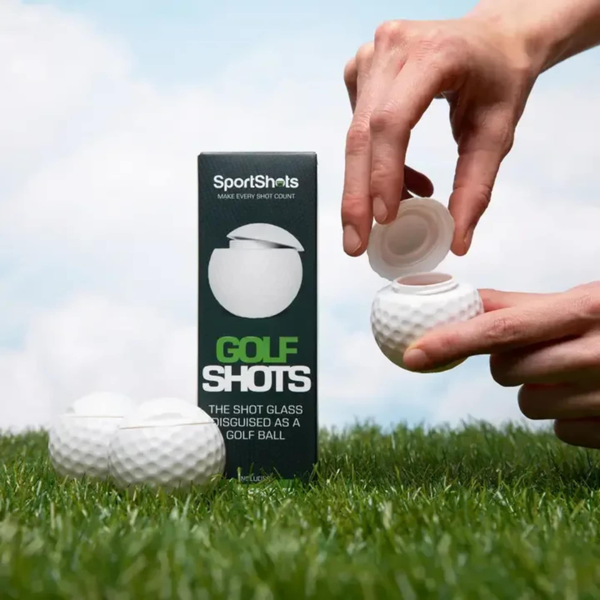 Golf ball-shaped shot glass held open beside its box on grass