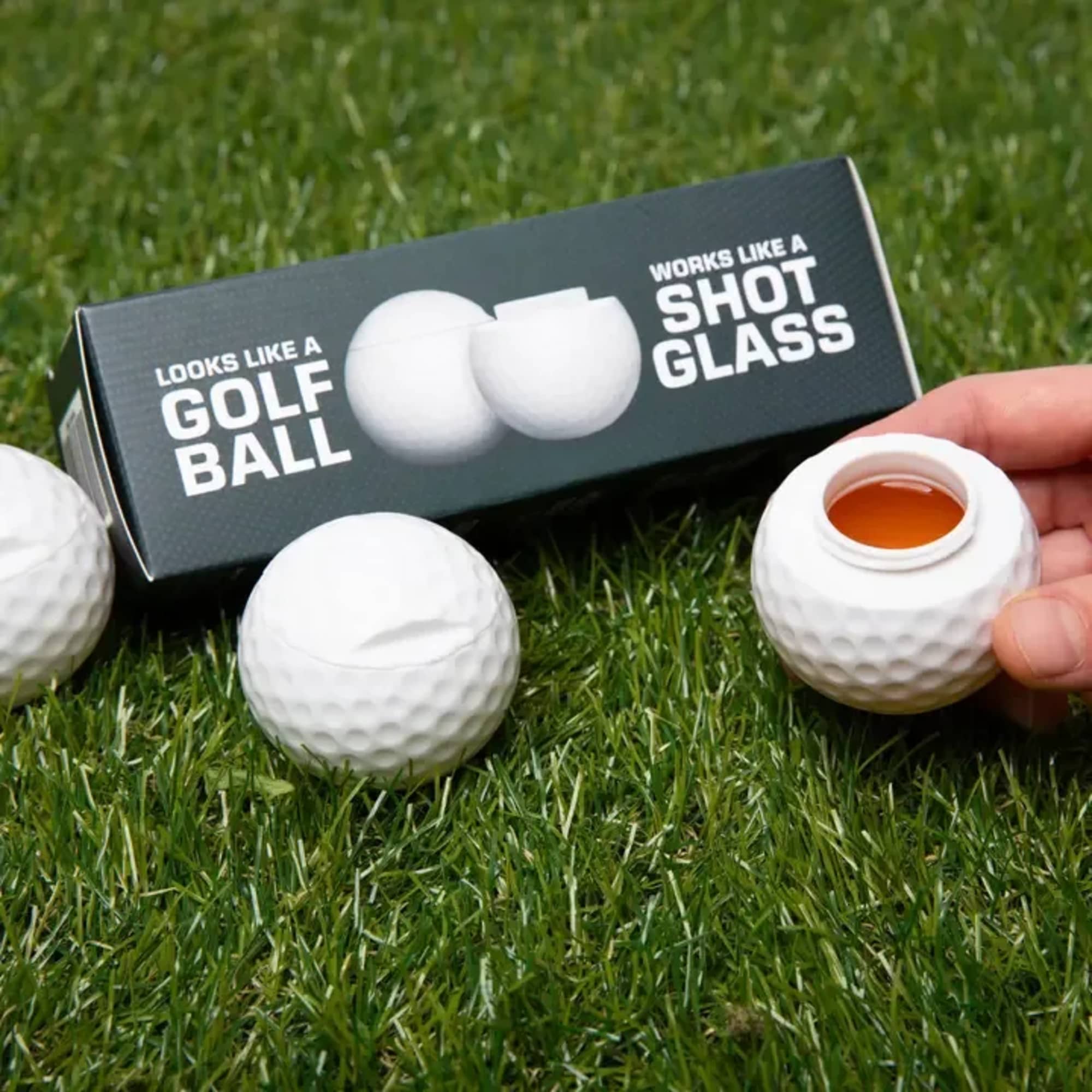 Golf-ball-shaped shot glasses on grass with a product box