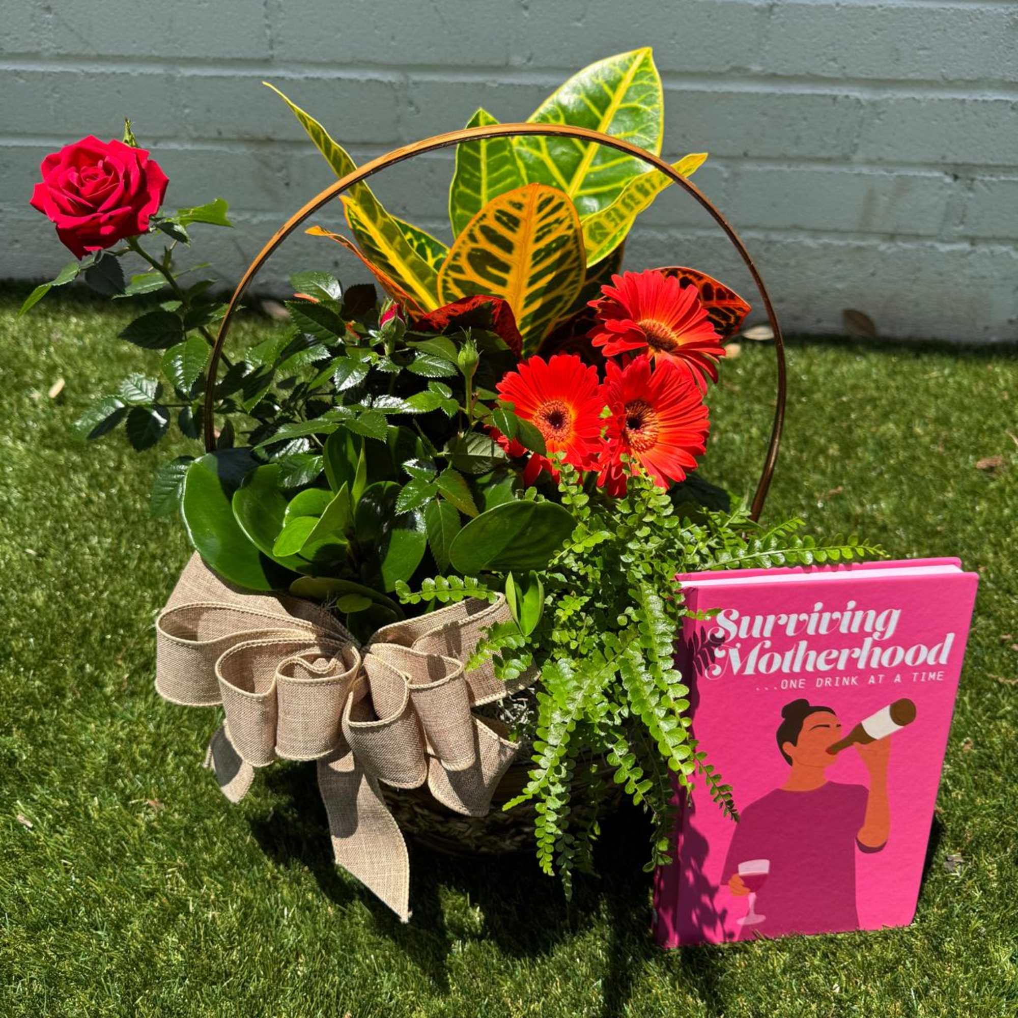 Basket arrangement with a red rose, orange gerberas, and a pink card