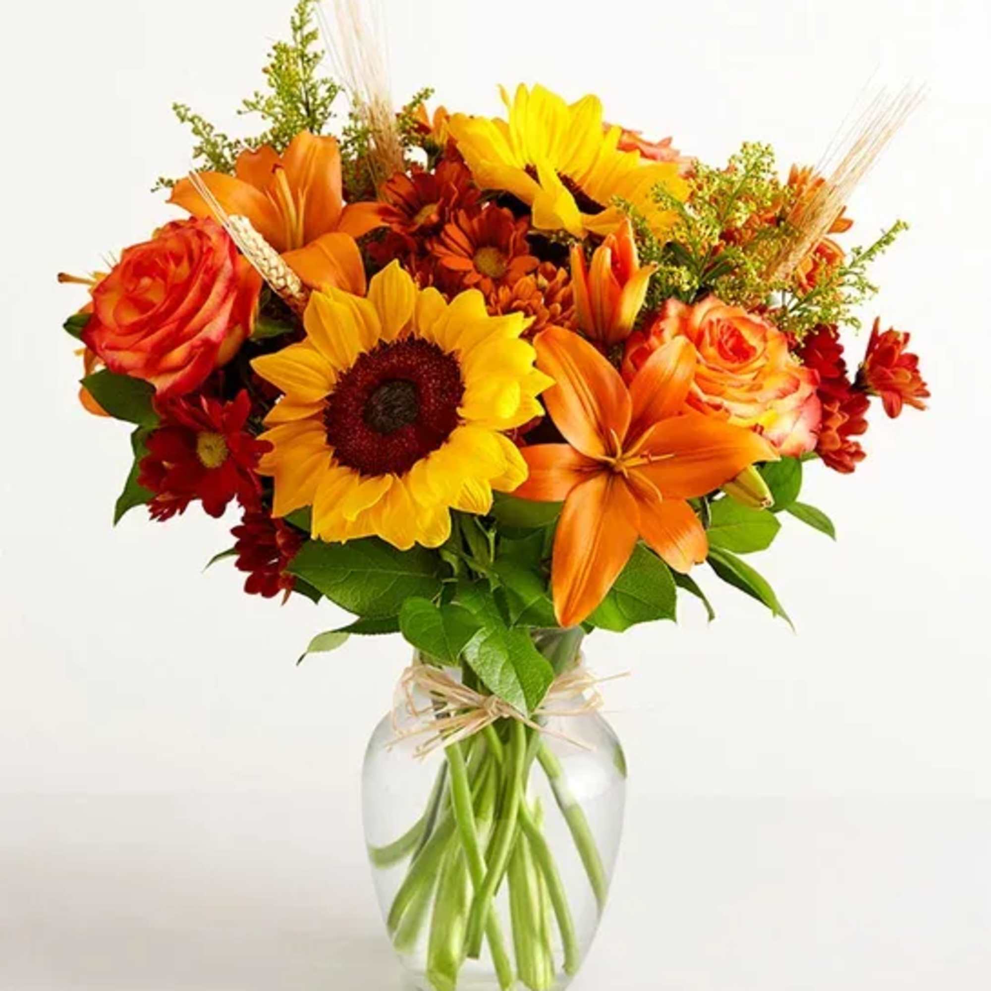 Bouquet of sunflowers, orange lilies, and roses in a clear glass vase