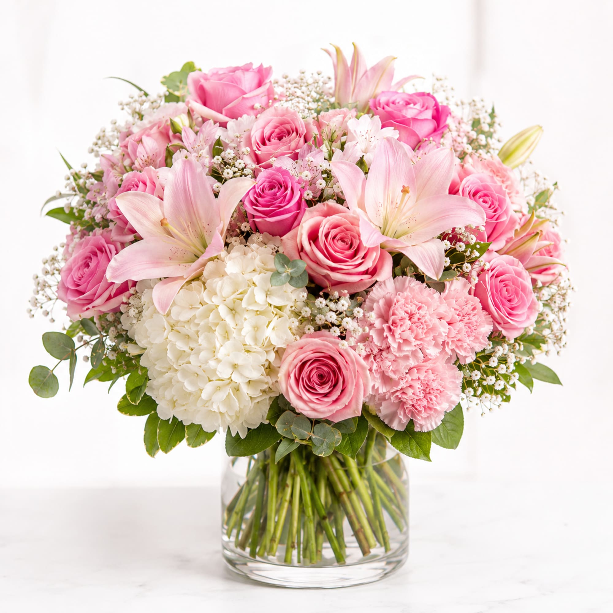 Soft blush roses and pale pink lilies form a rounded, romantic bouquet