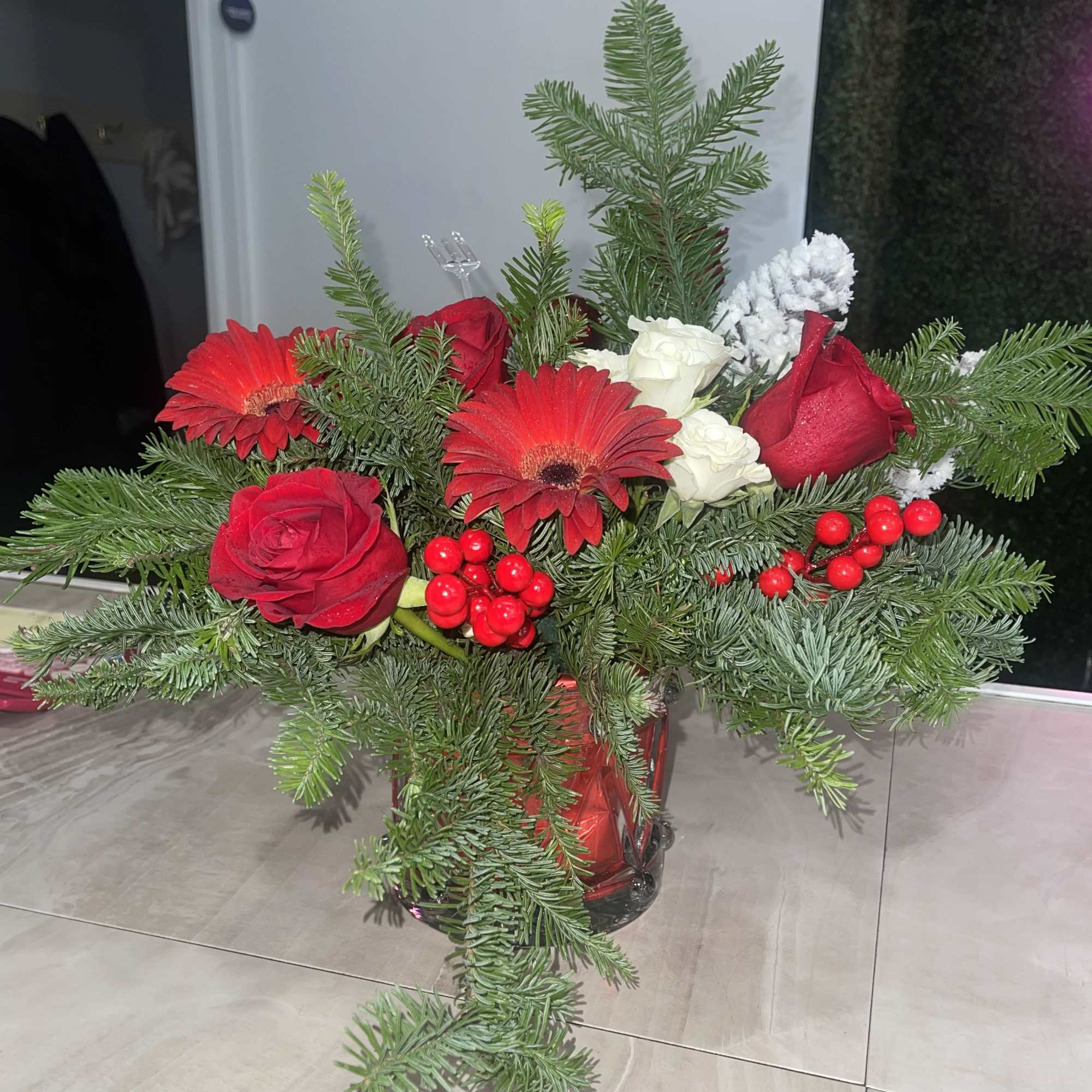 Red roses and gerbera daisies in a glass vase with evergreen branches