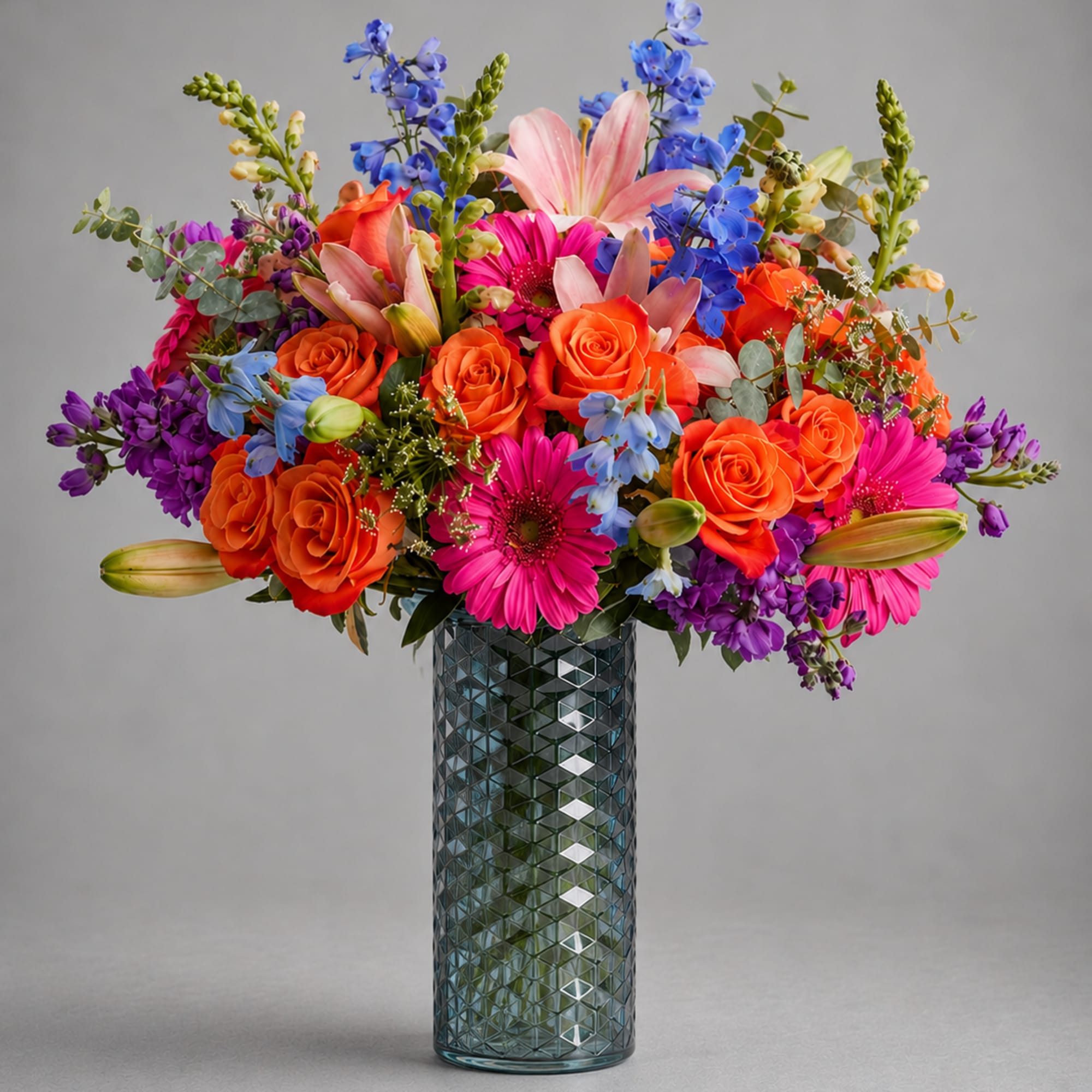 Bright mixed bouquet in a textured glass vase with roses, lilies, and daisies