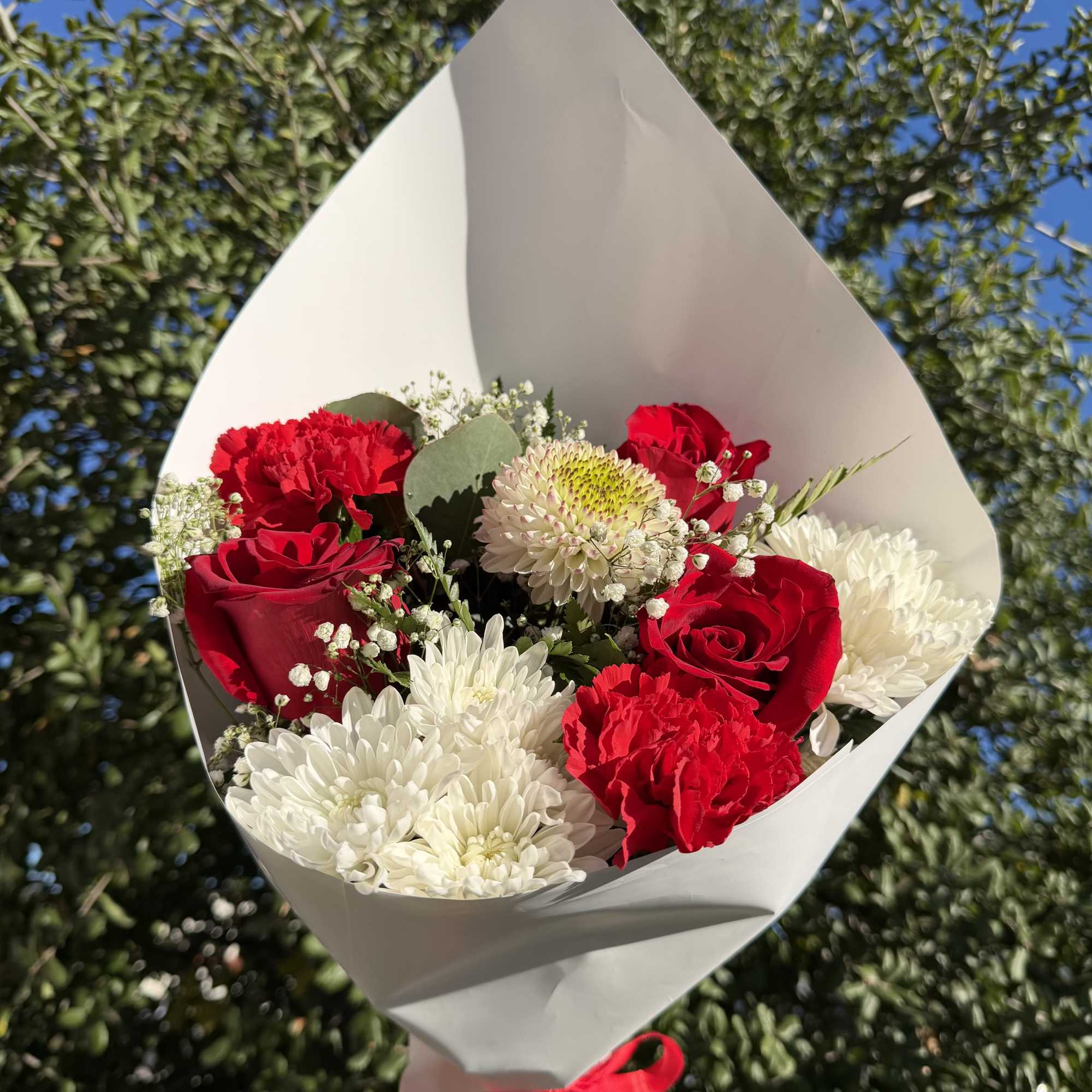 Bouquet of red roses, red carnations, and white chrysanthemums wrapped in white paper