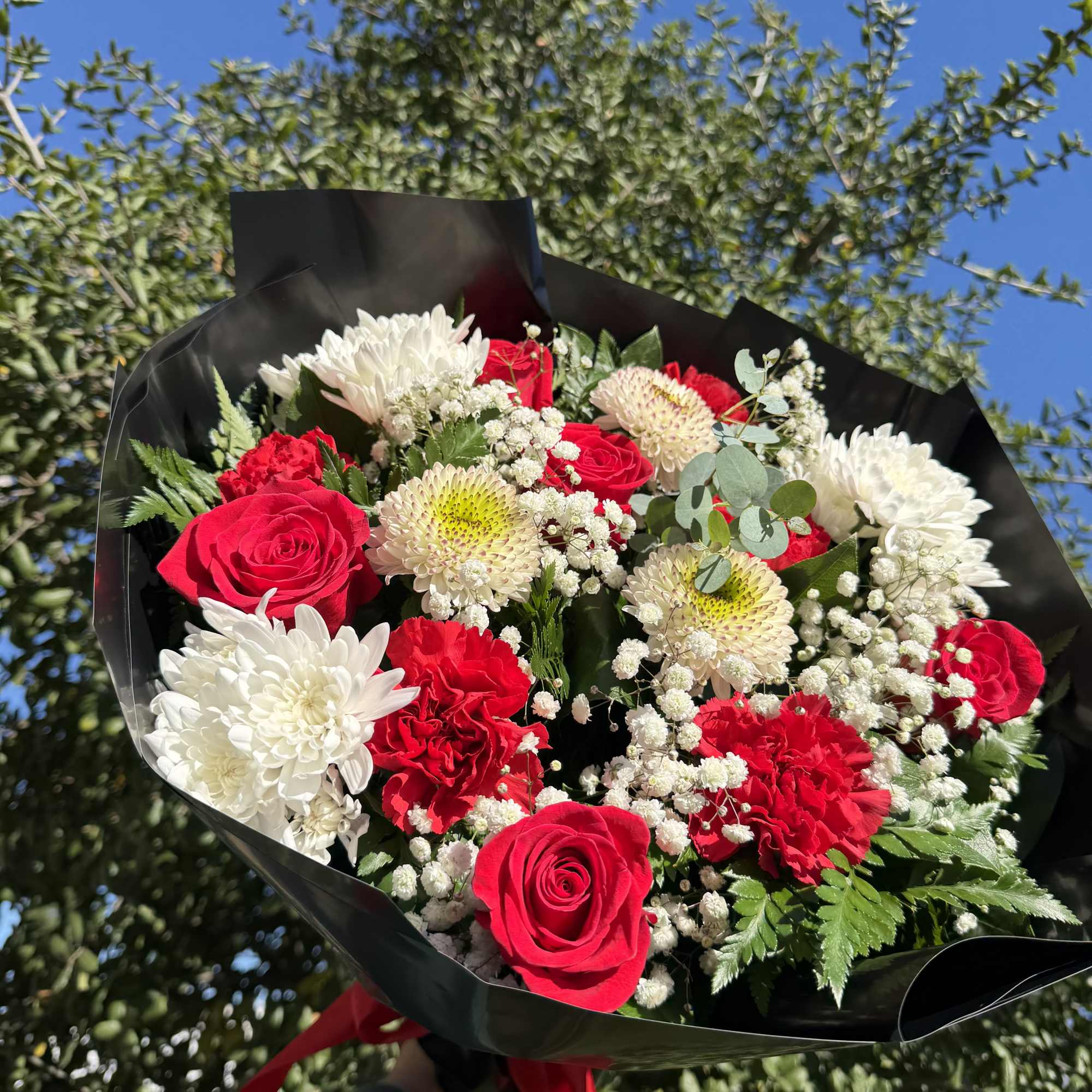 Bouquet of red roses and white chrysanthemums wrapped in black paper