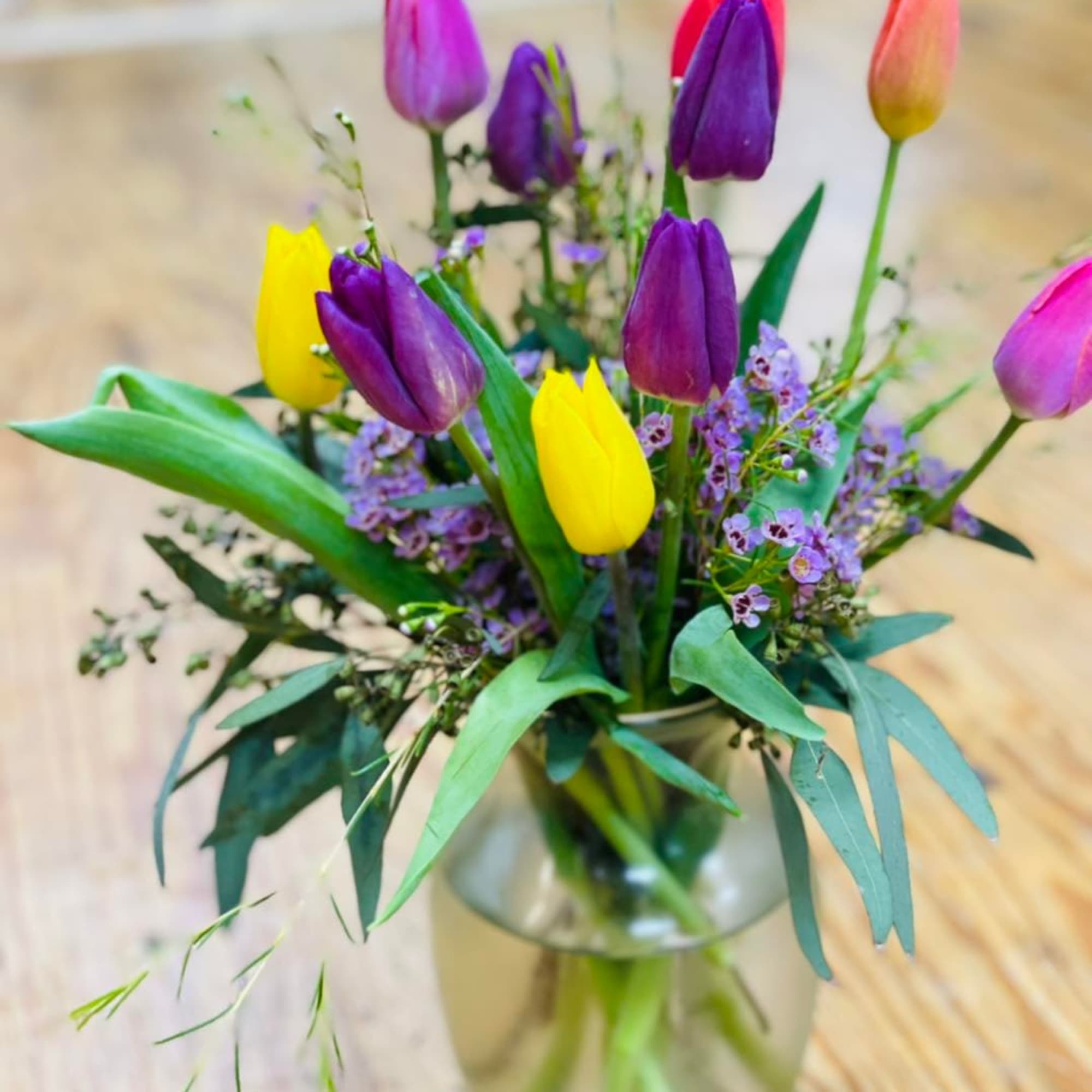 Mixed tulips in a clear glass vase with small purple filler flowers