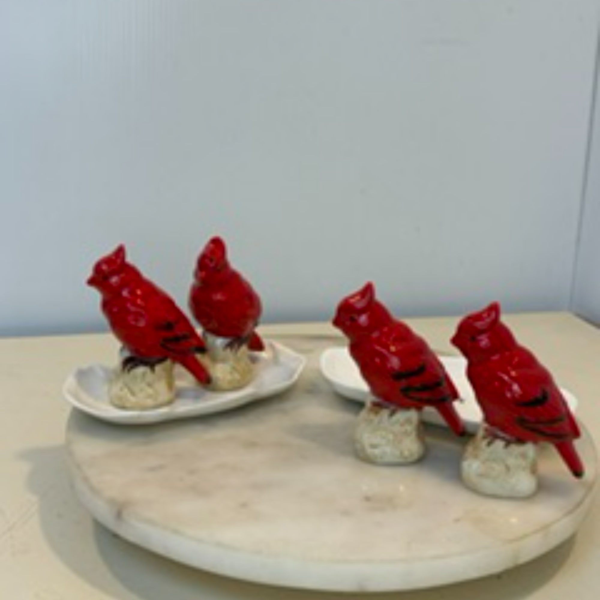 Four red bird figurines on small white bases arranged on a round tray