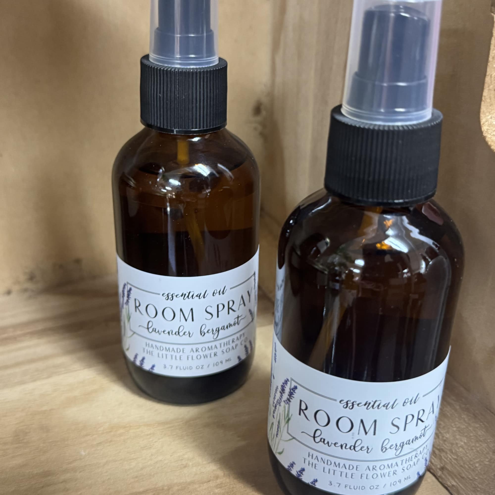 Two amber room spray bottles with black spray tops on a wooden shelf.