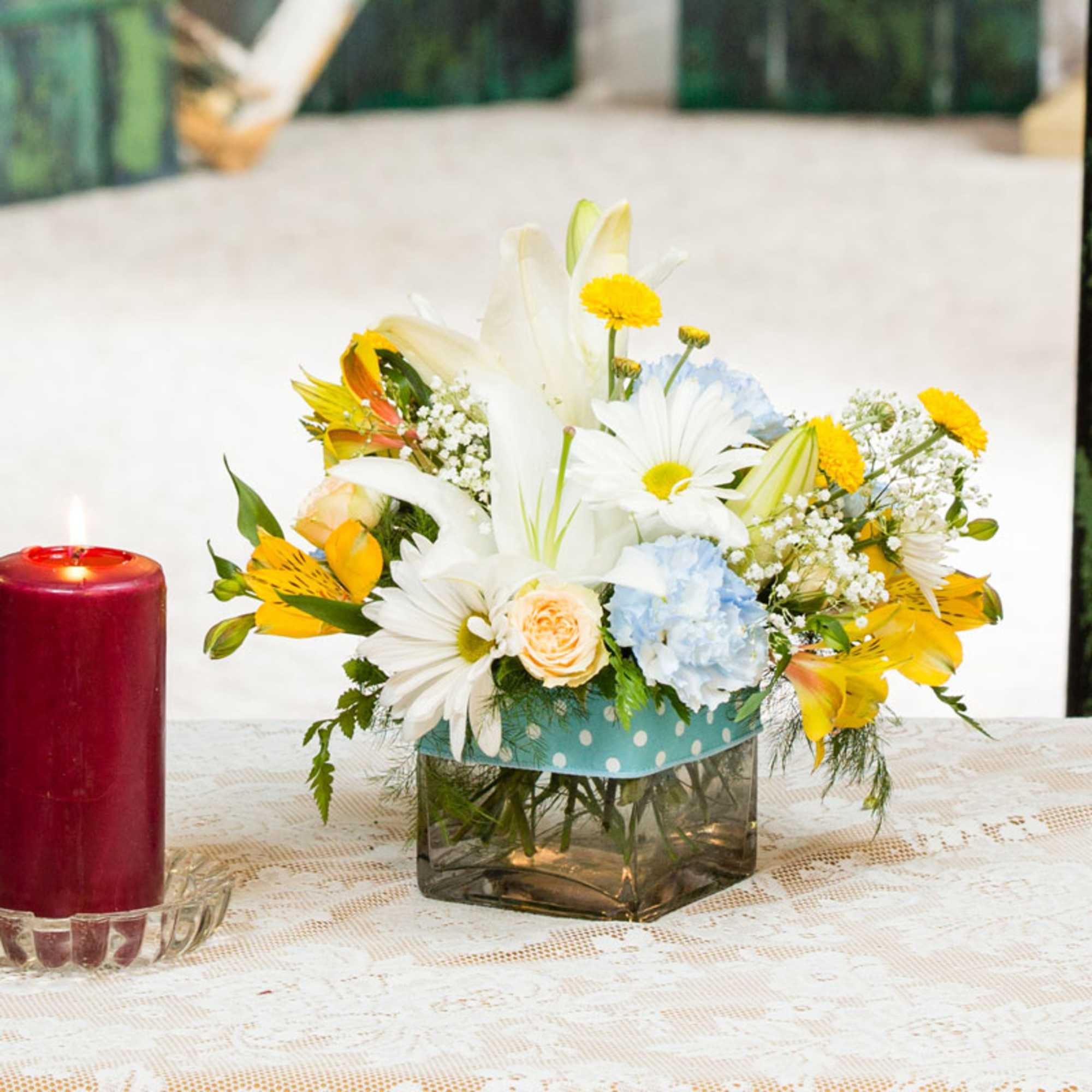 Mixed bouquet of white lilies, daisies, and yellow flowers in a square vase