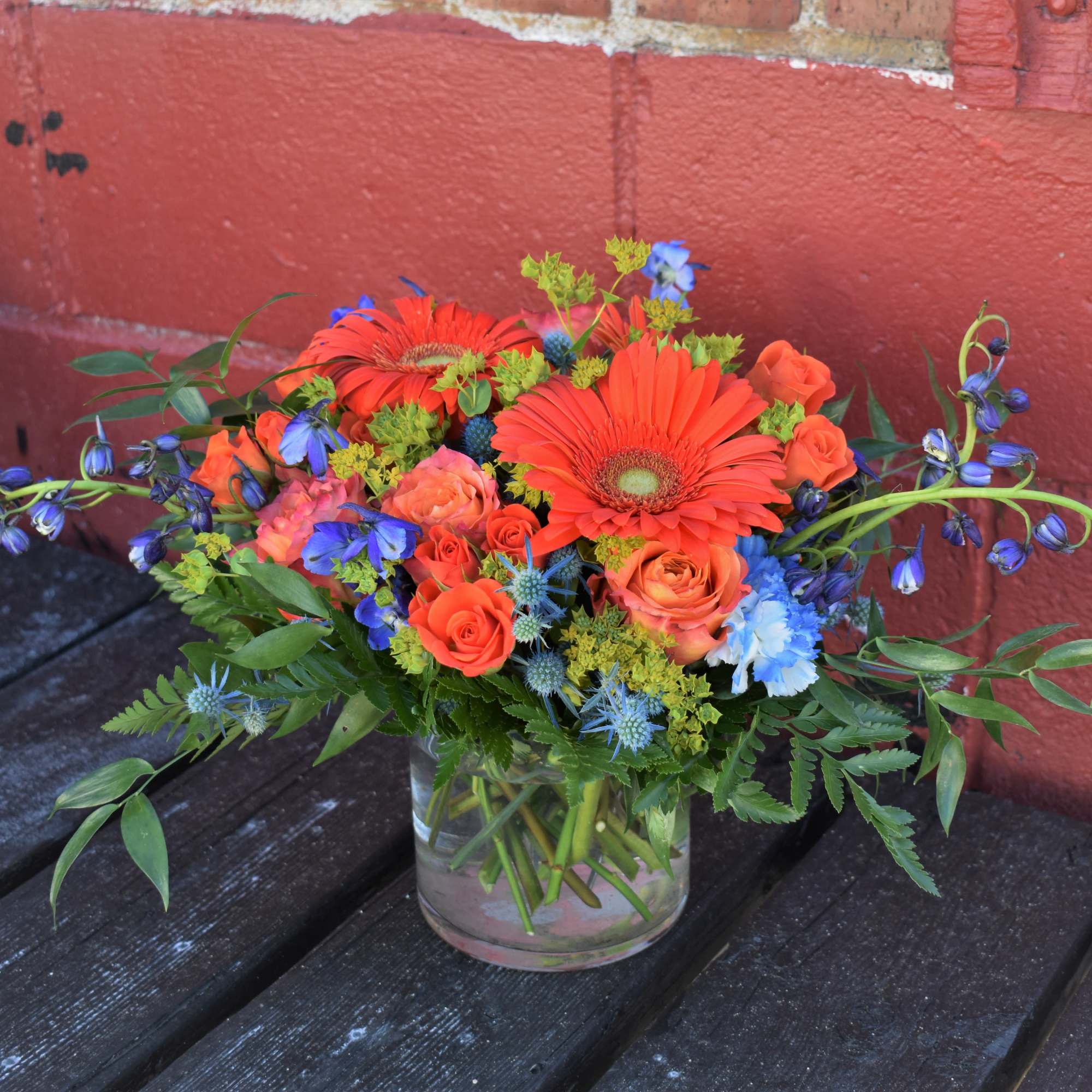 Orange gerbera daisies and roses in a clear glass vase