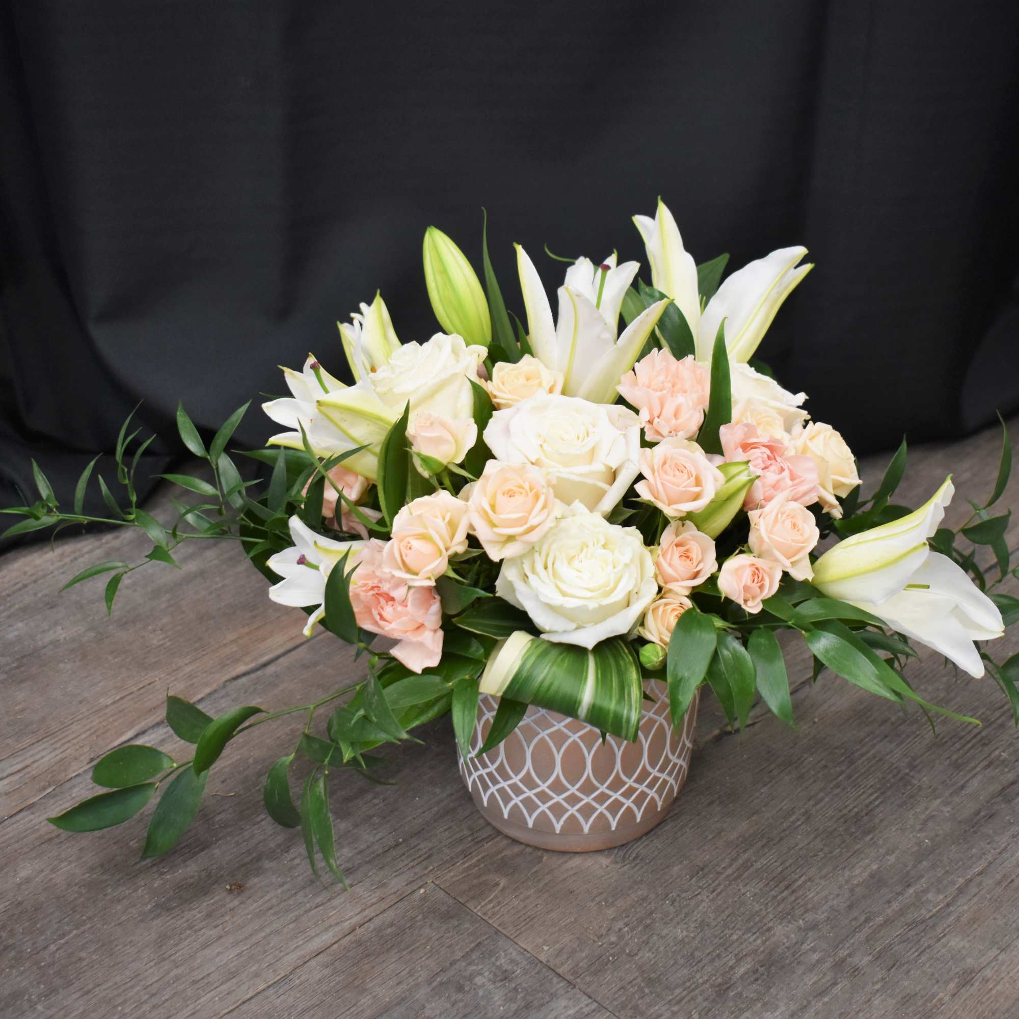 Low floral arrangement of white lilies and pale roses in a patterned vase