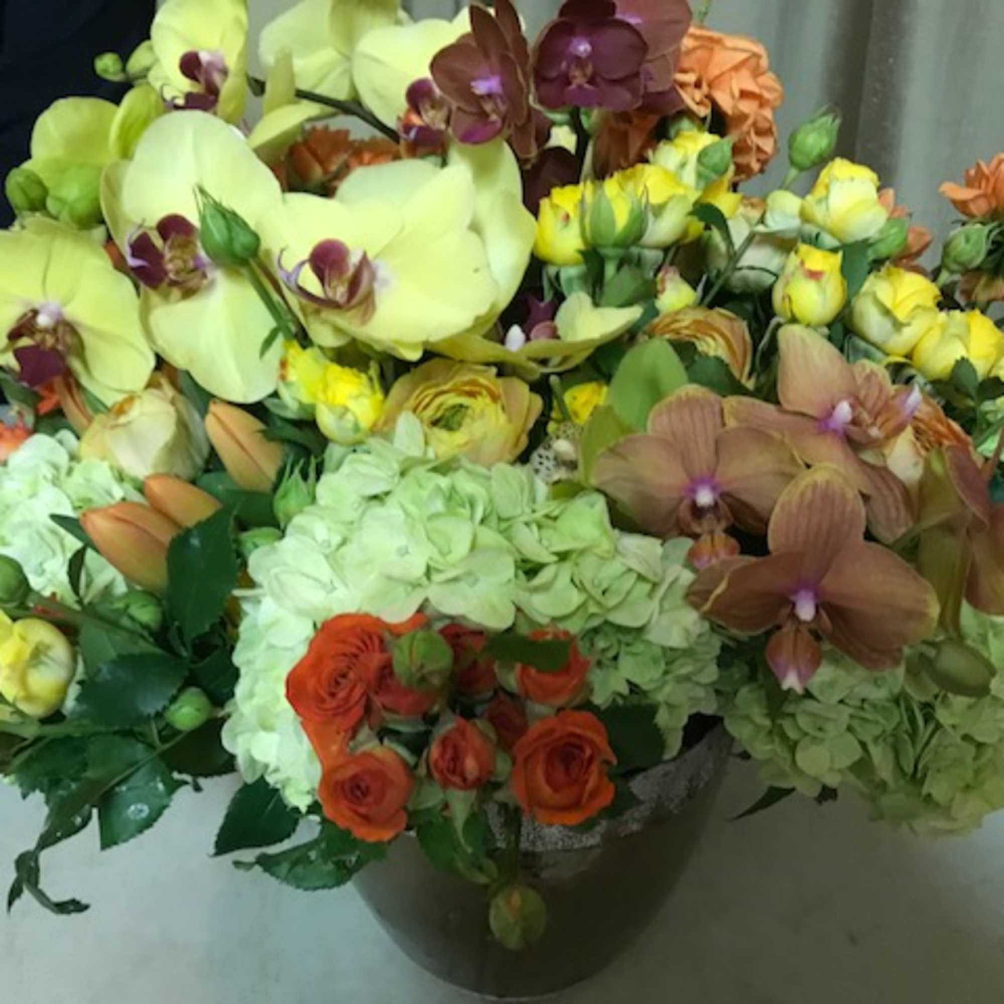 Mixed bouquet with orchids, hydrangeas, and roses in a dark vase