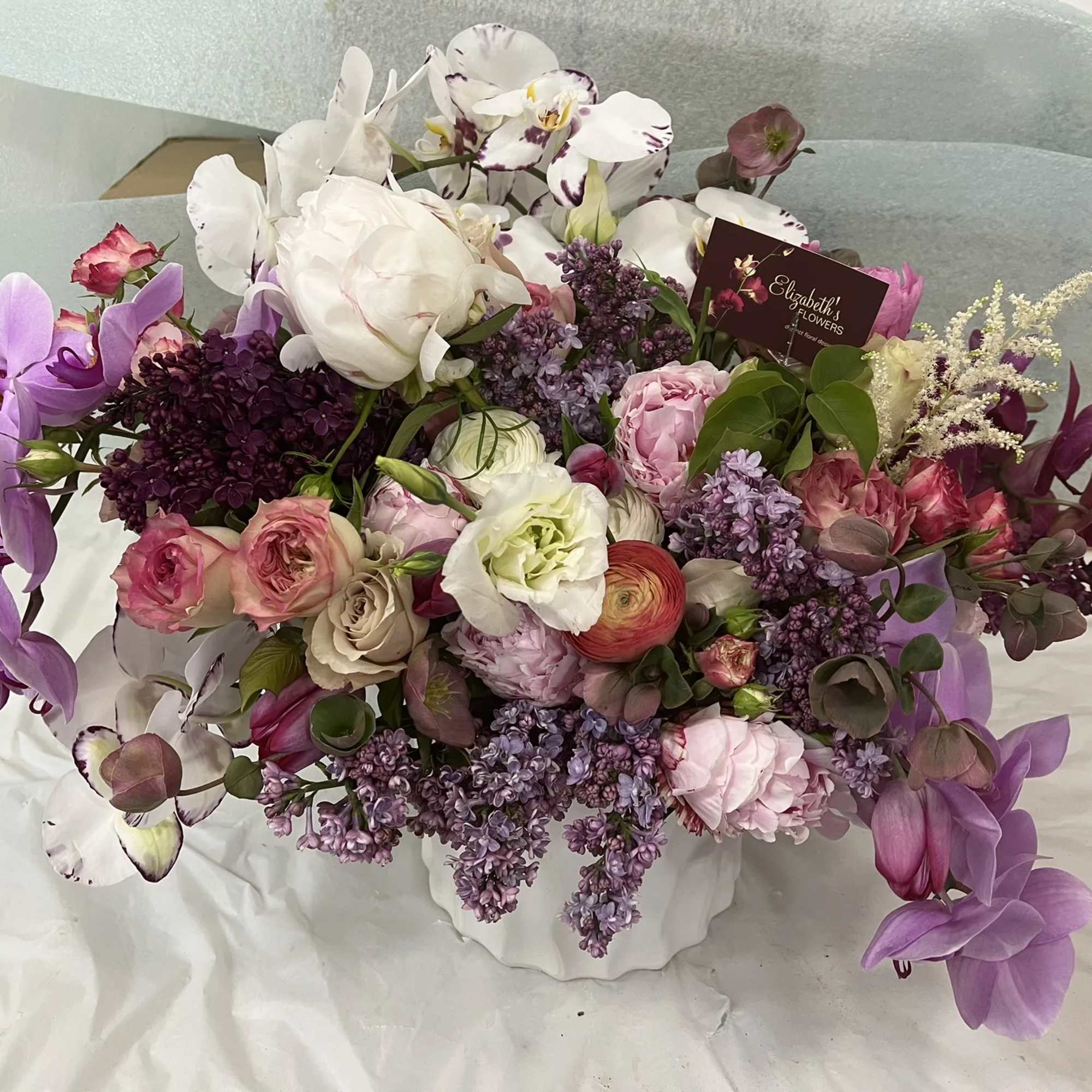 Lavender and white floral arrangement in a white container