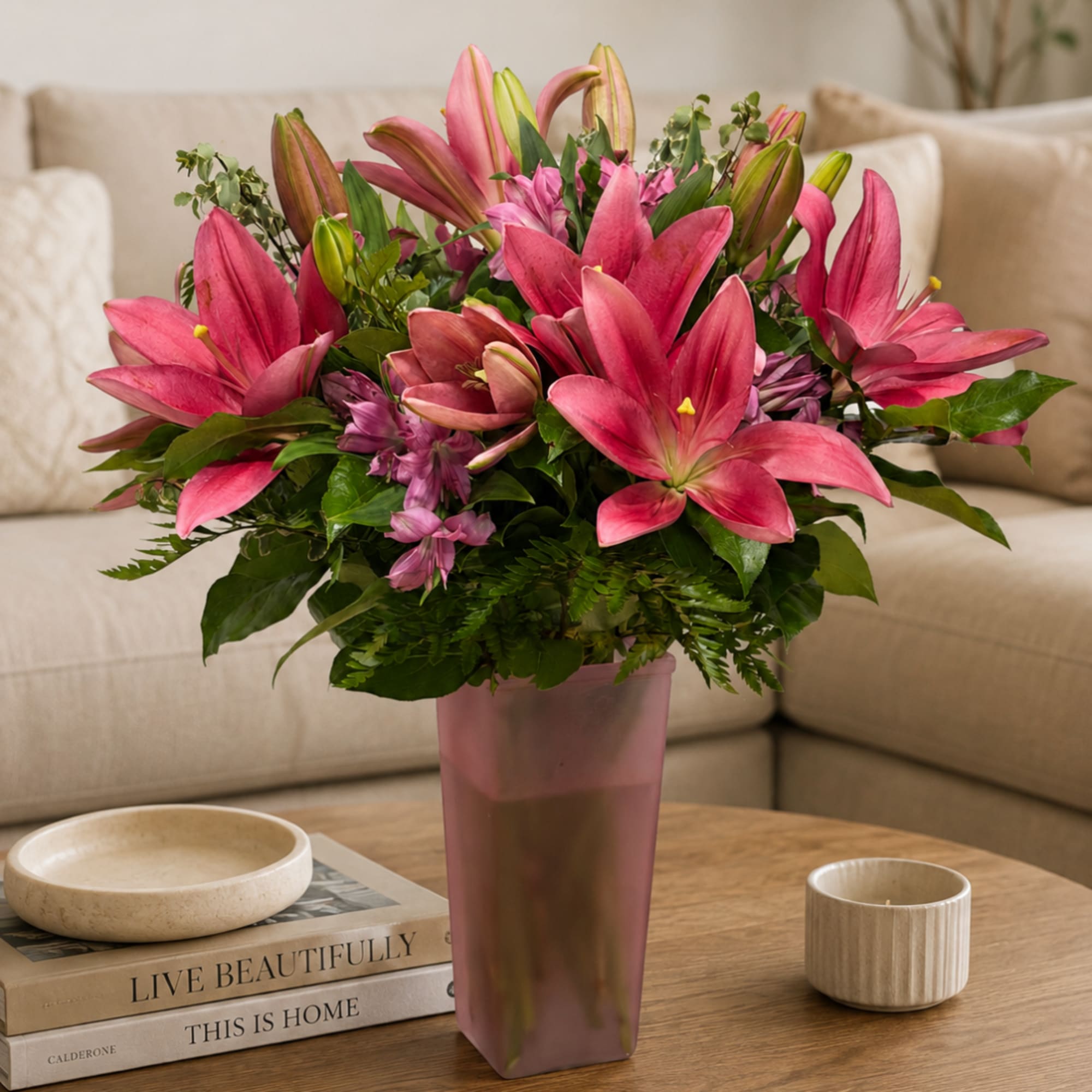 Pink lilies arranged in a tall vase on a coffee table