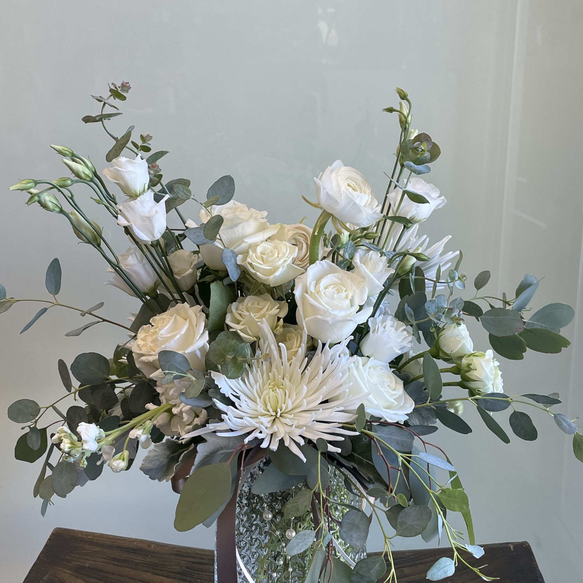 White roses and a chrysanthemum in a silver vase with eucalyptus