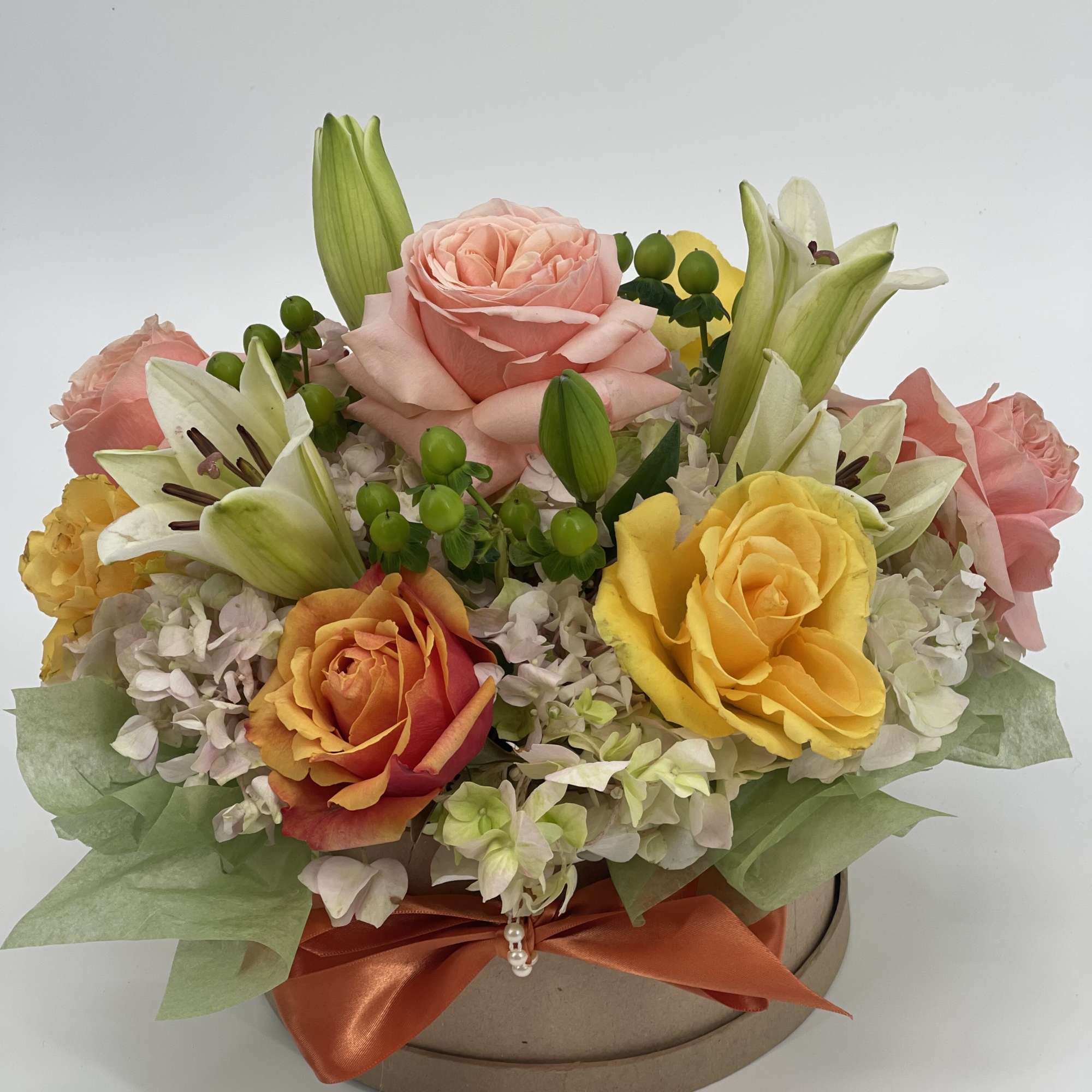 Bouquet of pink, yellow, and orange roses with white lilies in a round box