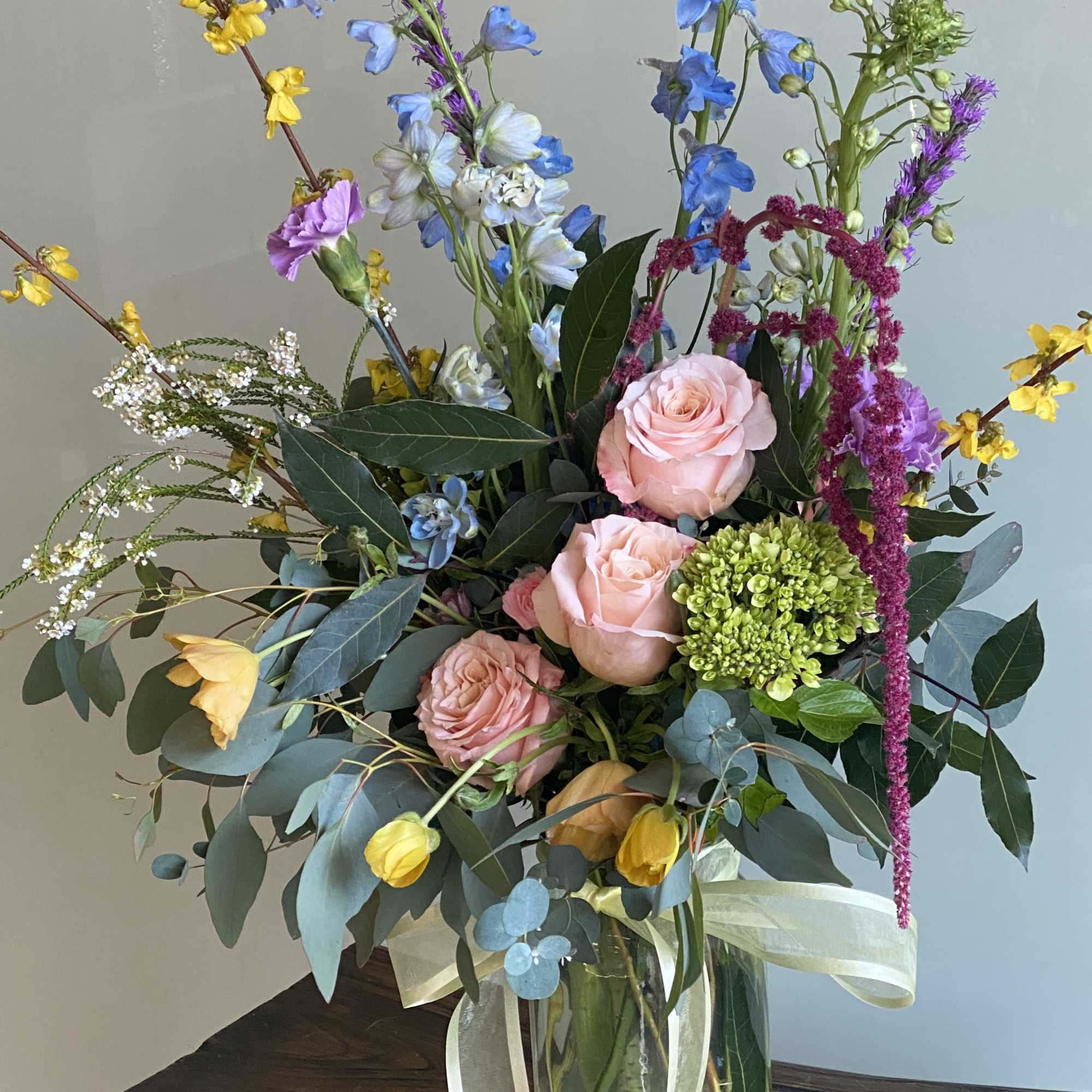 Tall mixed bouquet in a glass vase with pink roses and blue flowers