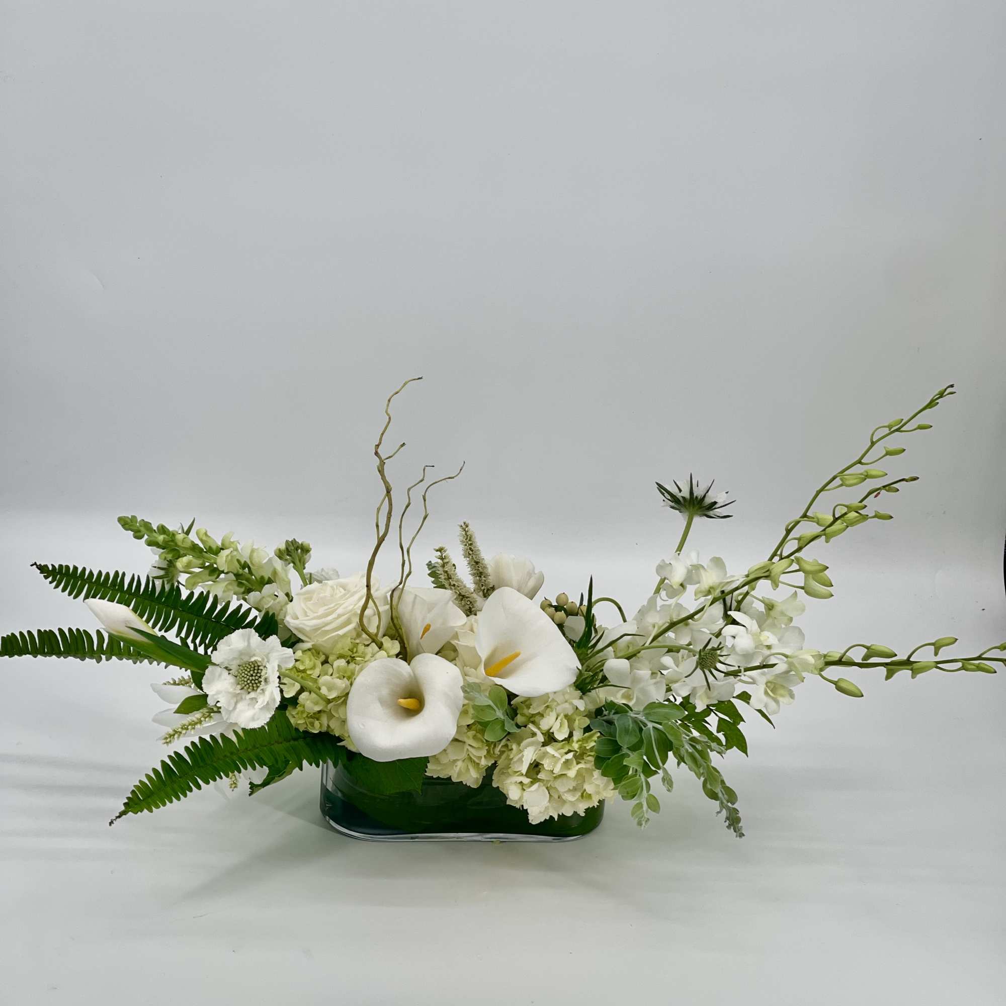 White floral arrangement in a green glass vase with calla lilies and orchids