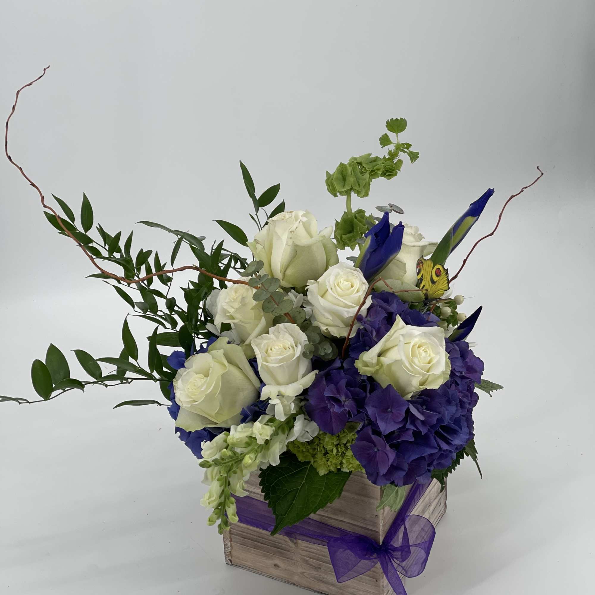 White roses and purple flowers arranged in a wooden box with a ribbon