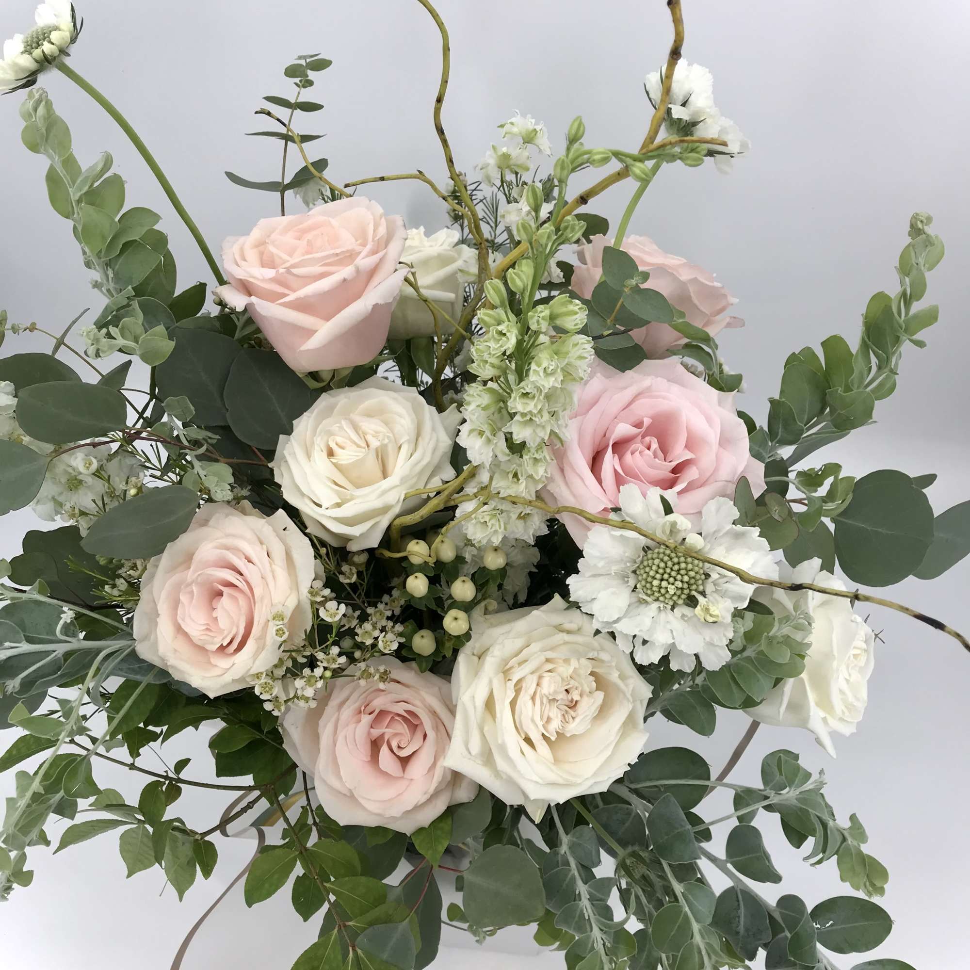 Loose arrangement of blush and white roses with white accent flowers in a vase with trailing foliage