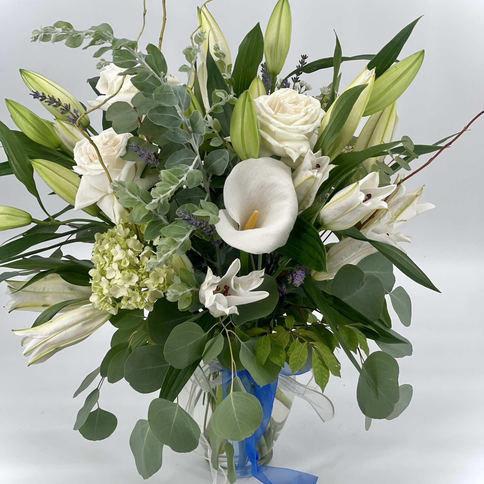 White roses and calla lilies in a glass vase with greenery