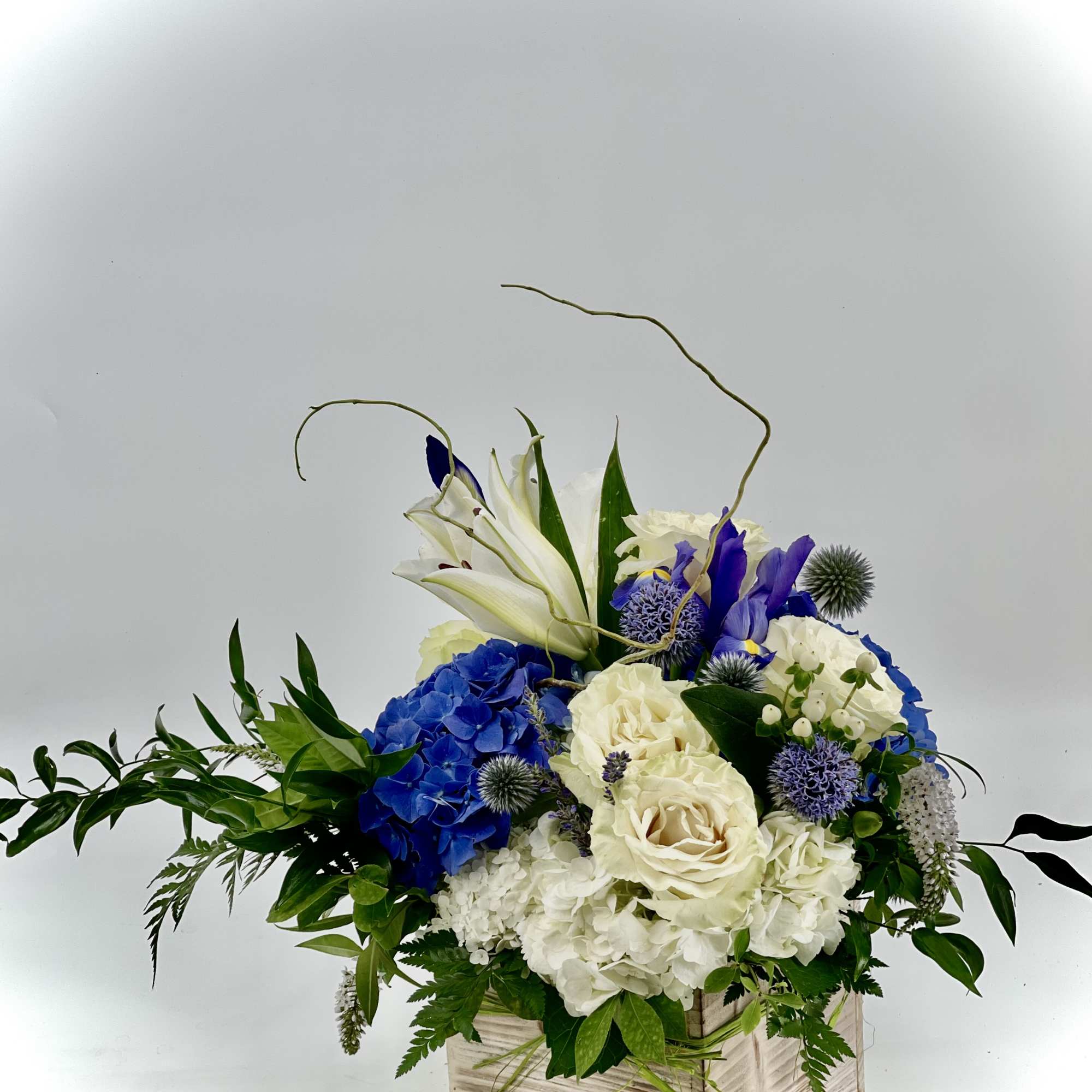 Blue and white floral arrangement in a wooden box with tall accent stems