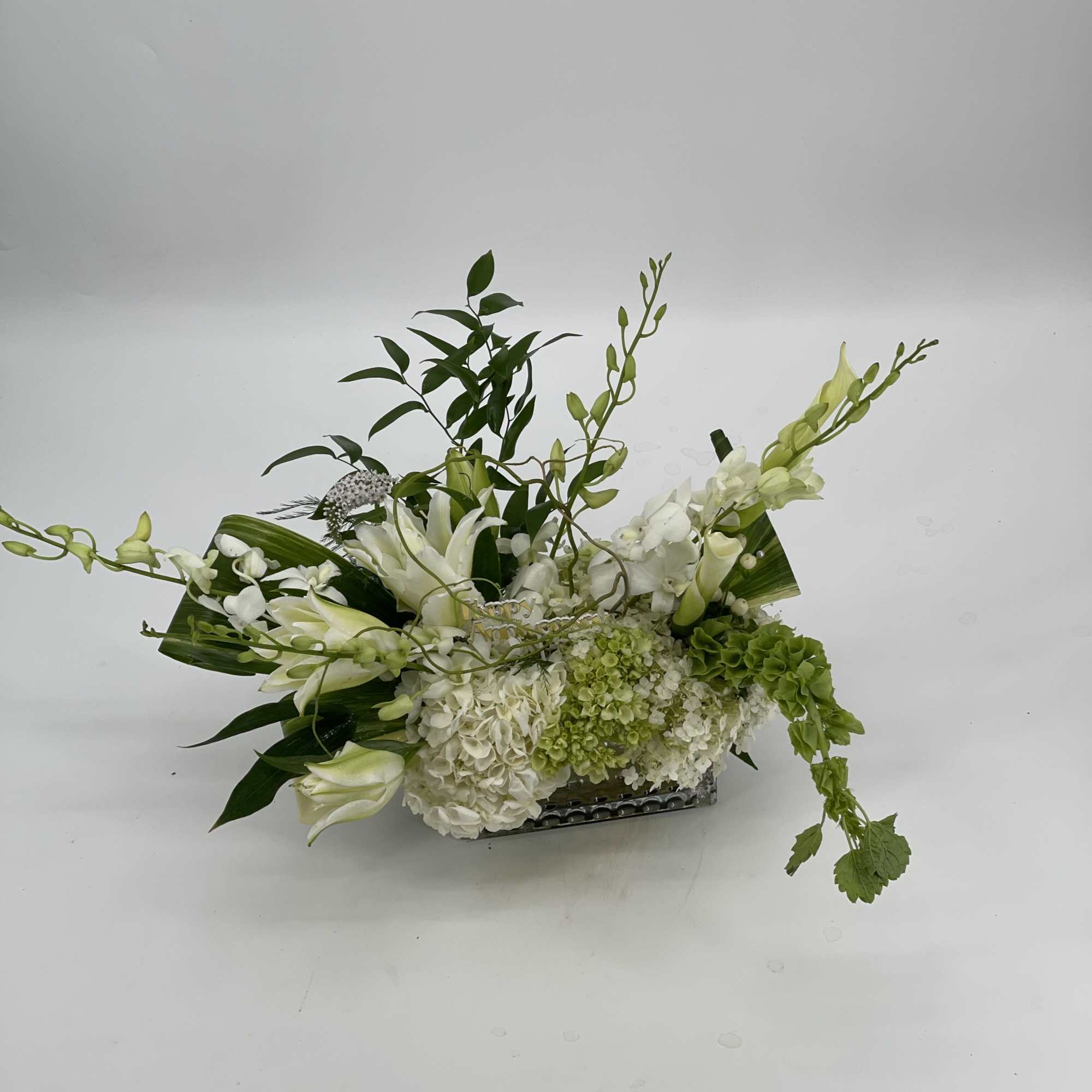 White floral arrangement with orchids and lilies in a low rectangular container