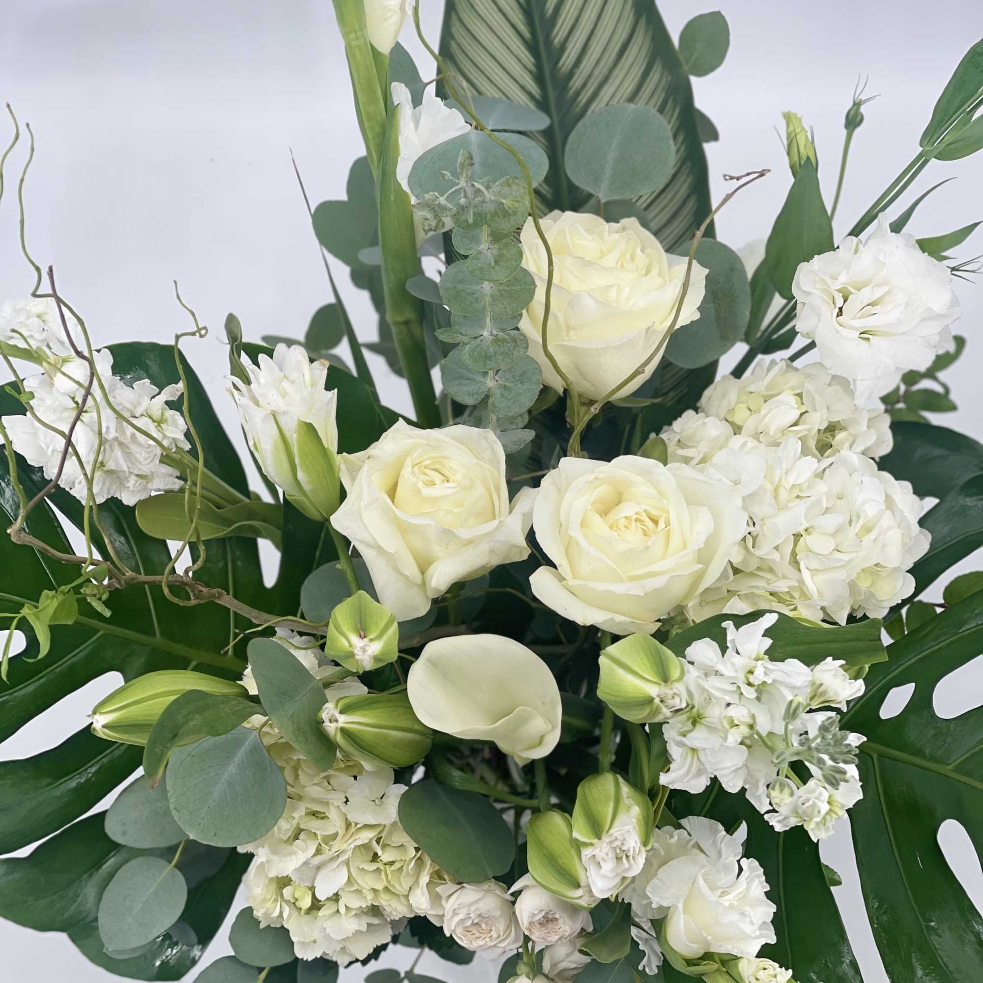 White roses and calla lilies arranged with eucalyptus and broad tropical leaves