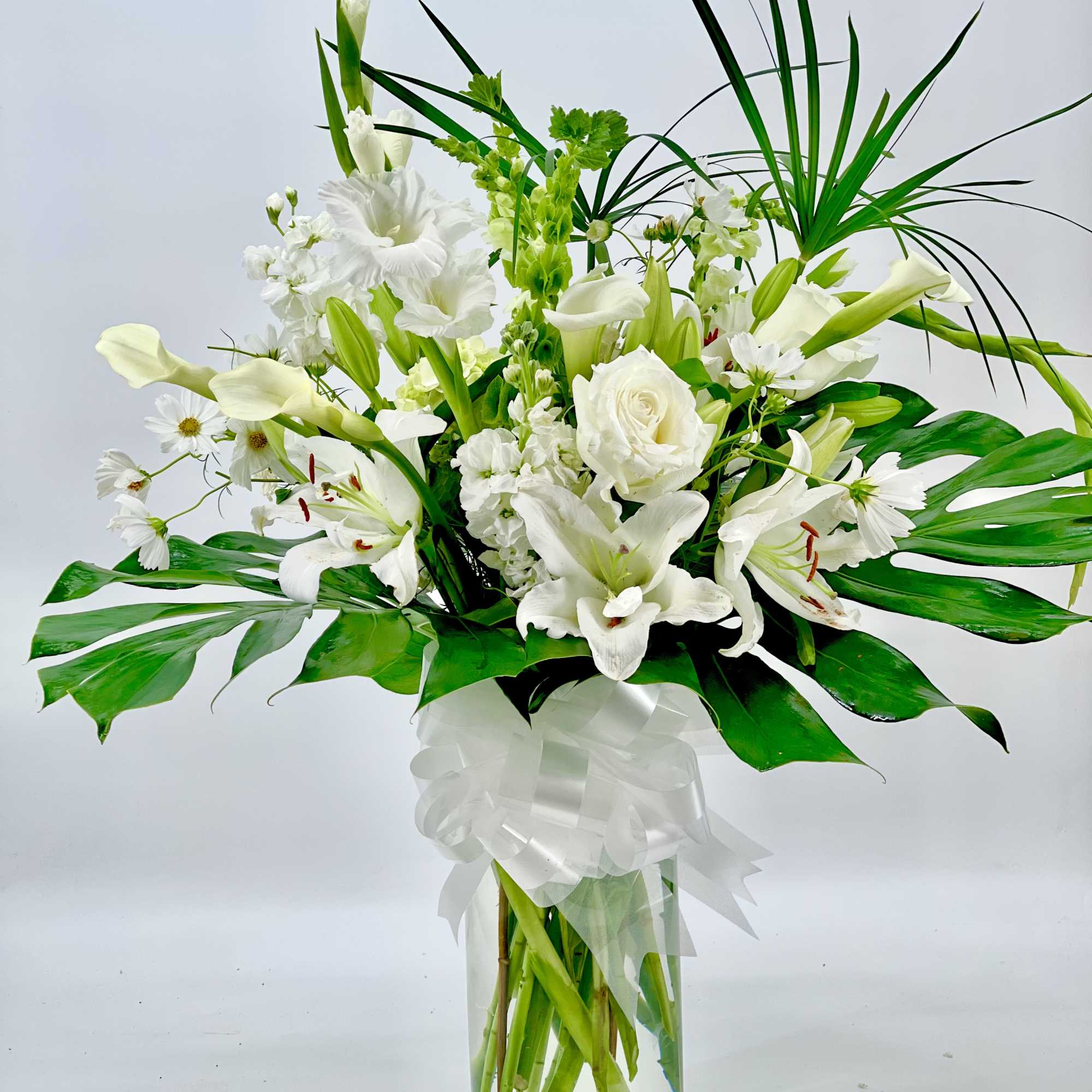 White floral arrangement in a clear glass vase with a white ribbon