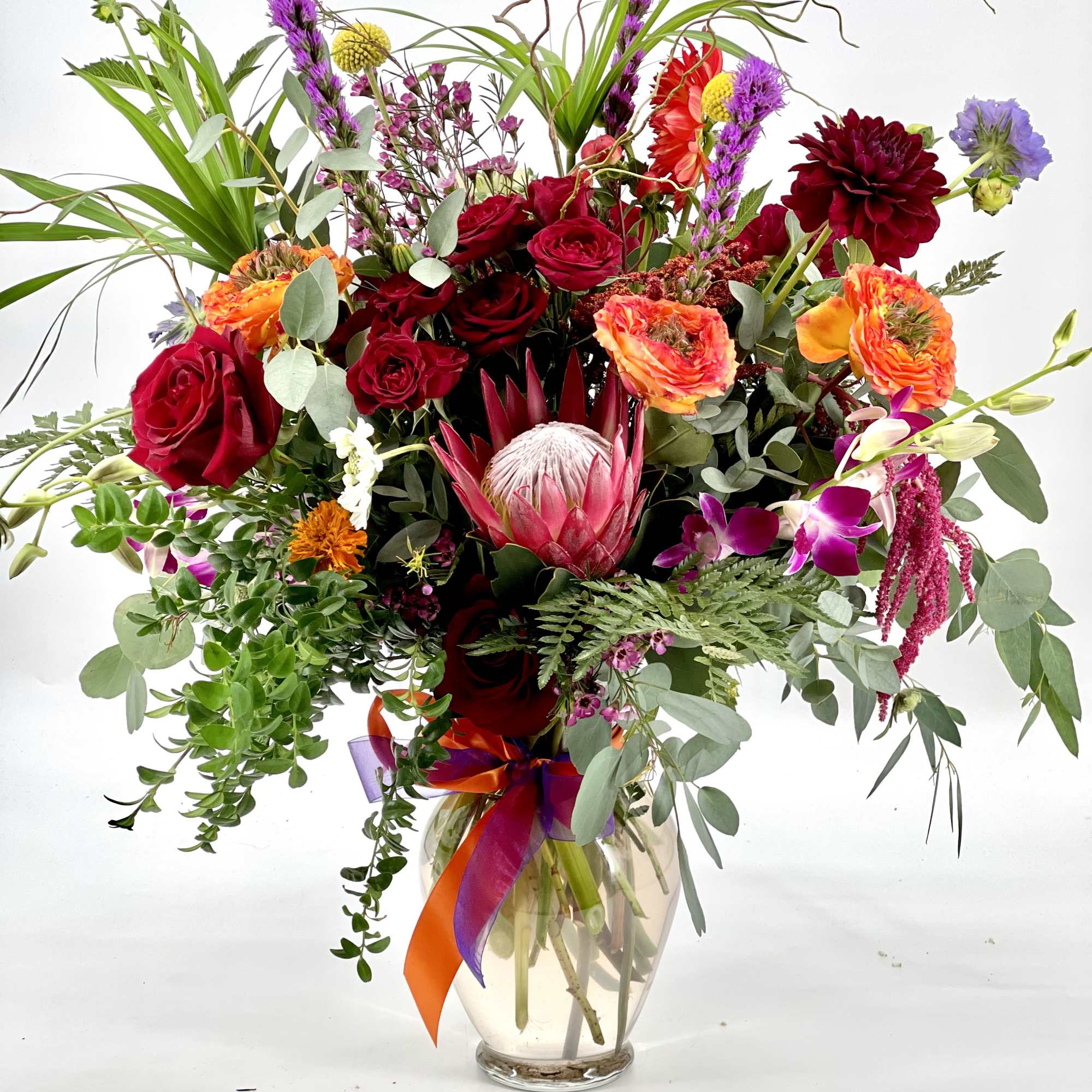 Mixed bouquet of red, orange, and purple flowers in a glass vase
