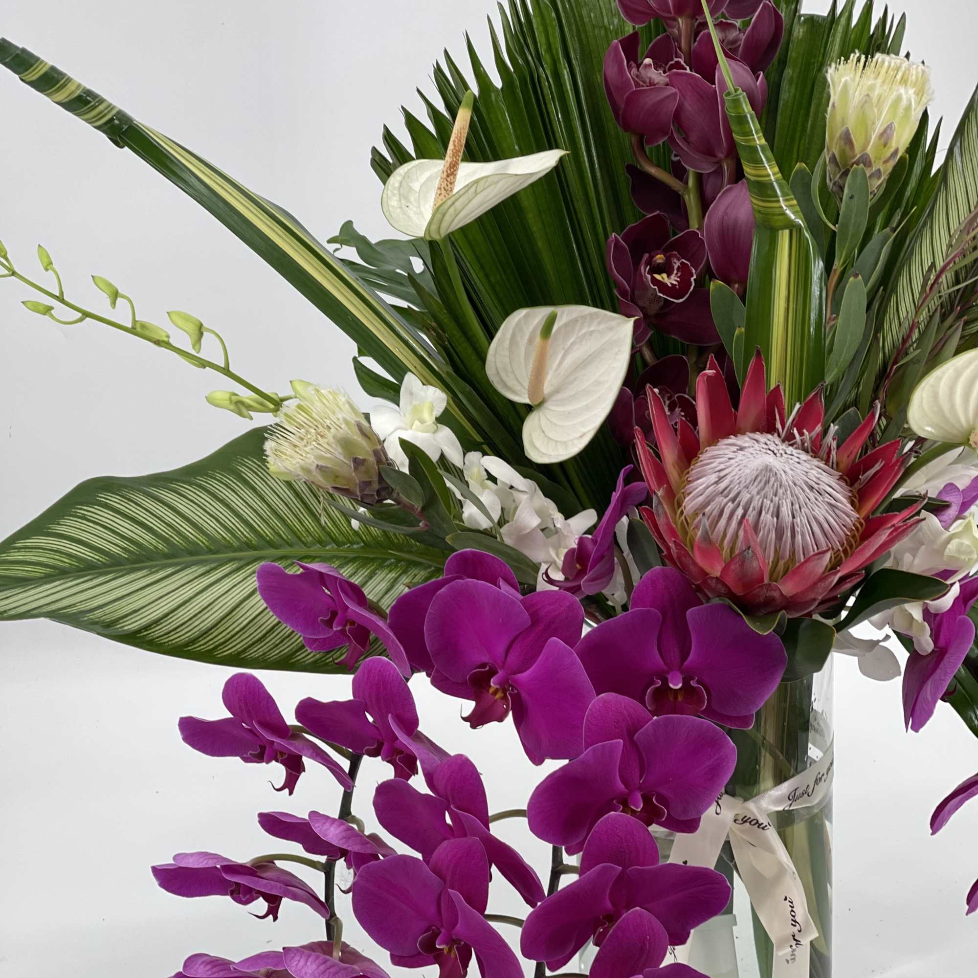 Tropical bouquet with purple orchids and white anthuriums in a glass vase