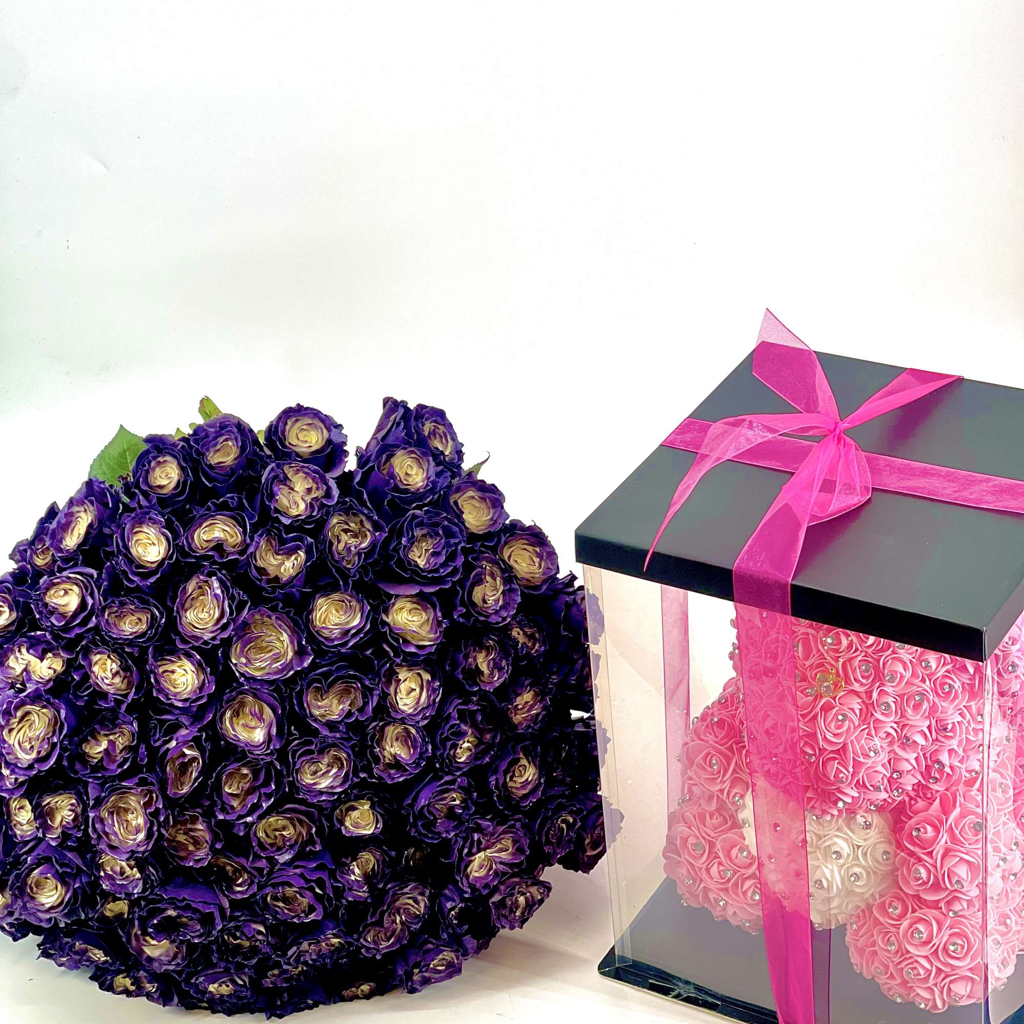 Purple rose bouquet beside a clear gift box tied with pink ribbon