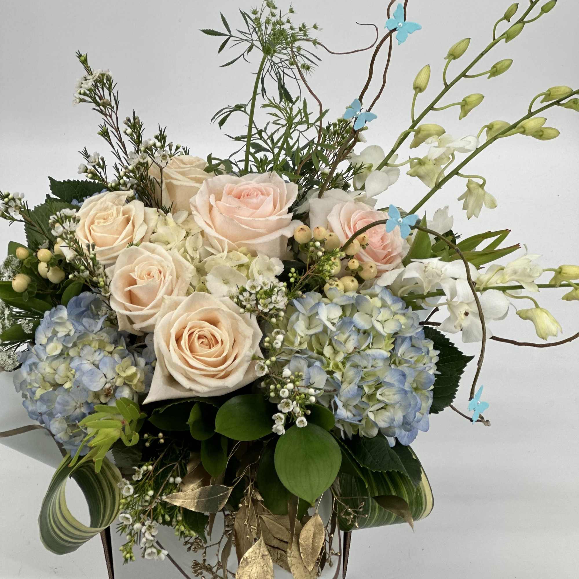 Arrangement of pale roses and blue hydrangeas in a decorative container
