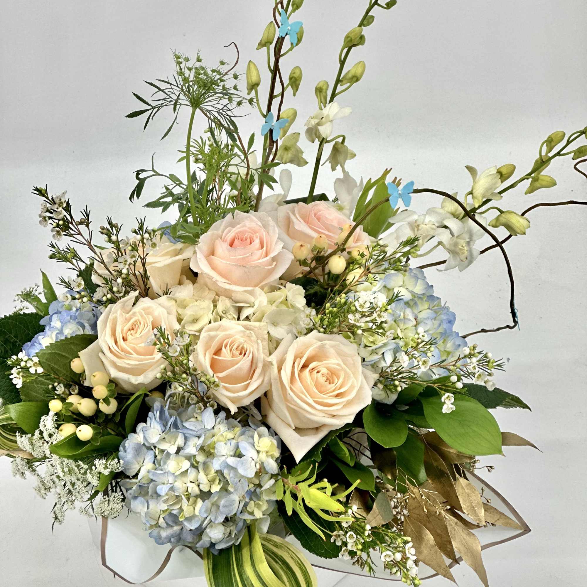 Bouquet of pale peach roses and blue hydrangeas with tall orchid stems