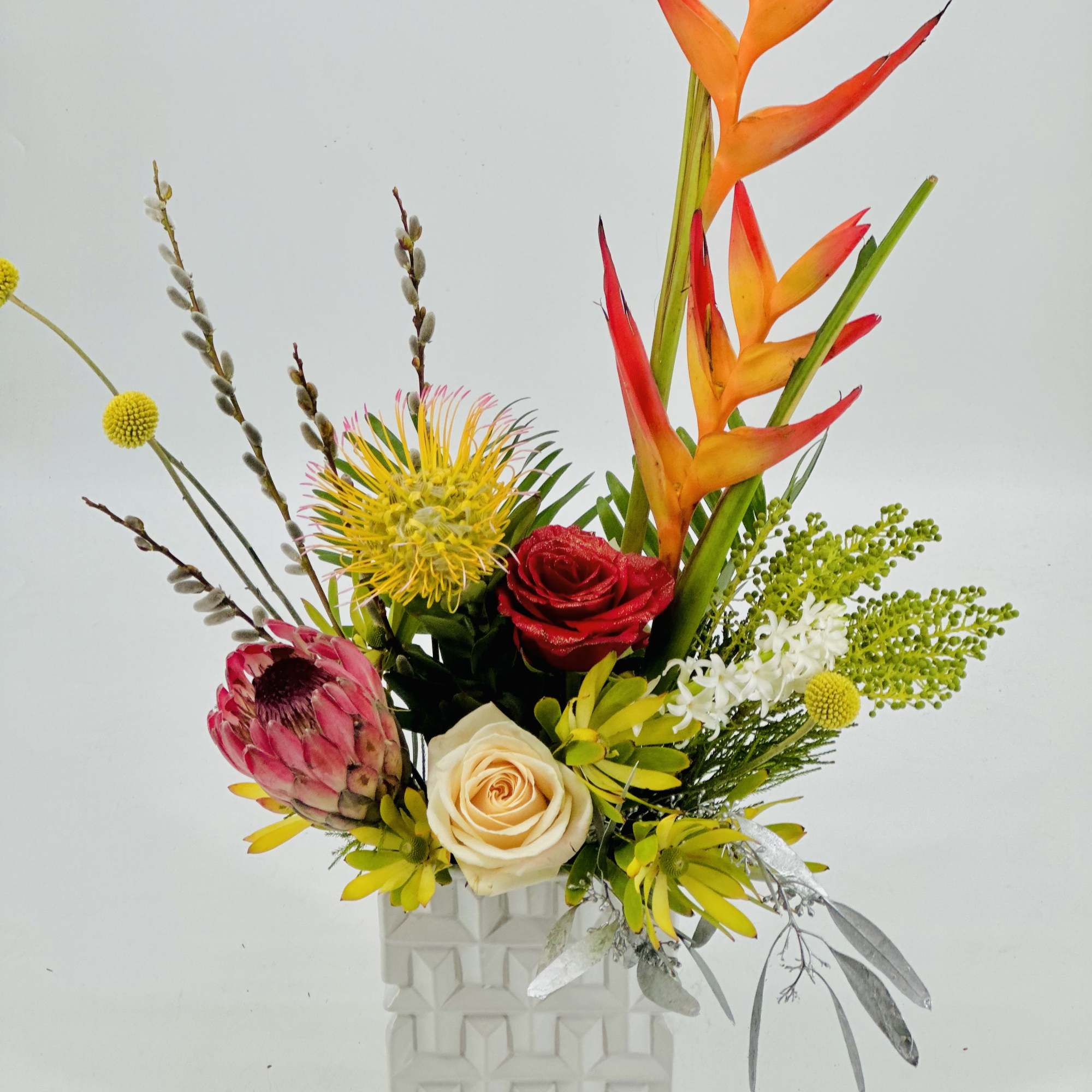 Tropical flower arrangement in a white geometric vase with orange heliconia and roses
