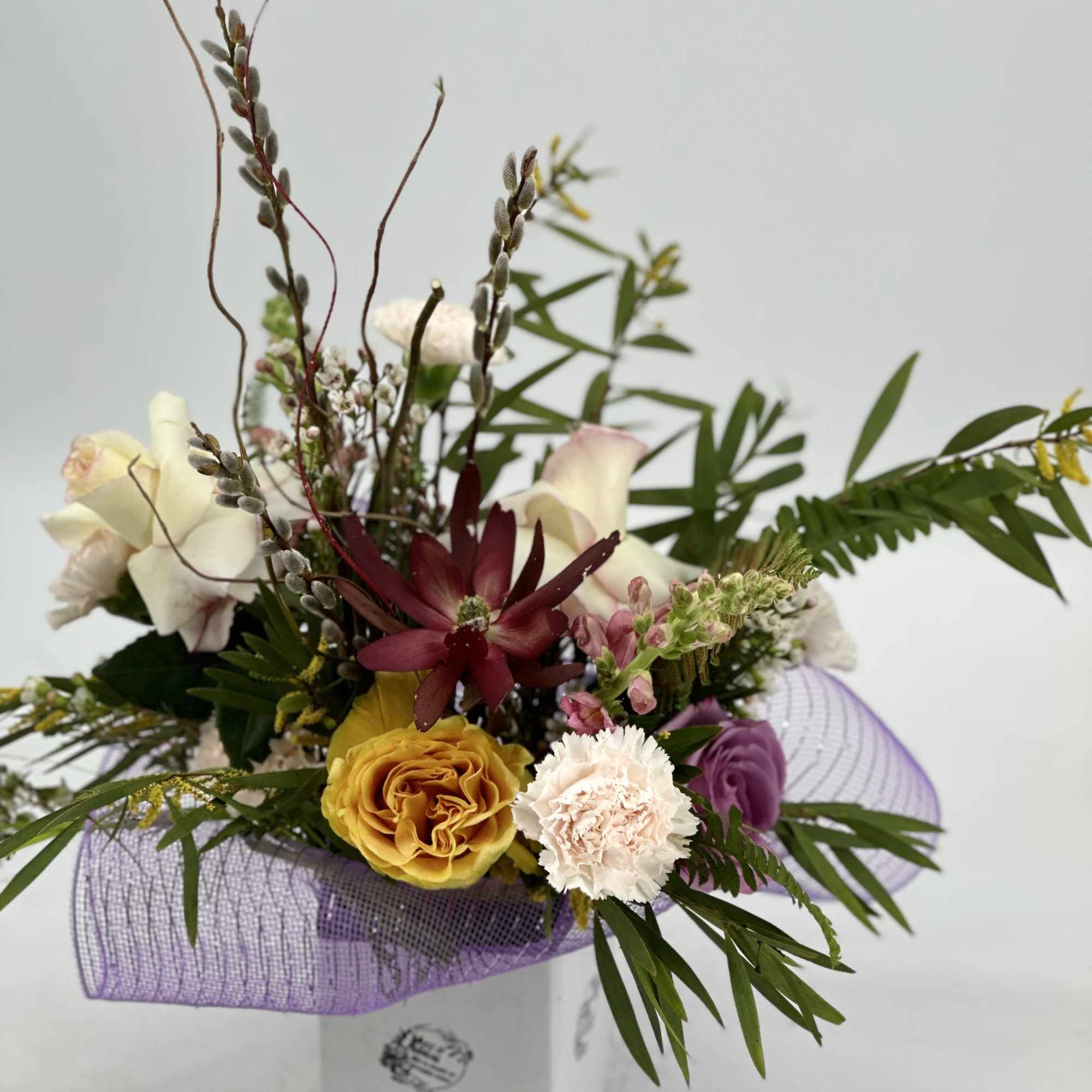 Mixed floral arrangement in a white box with purple wrap
