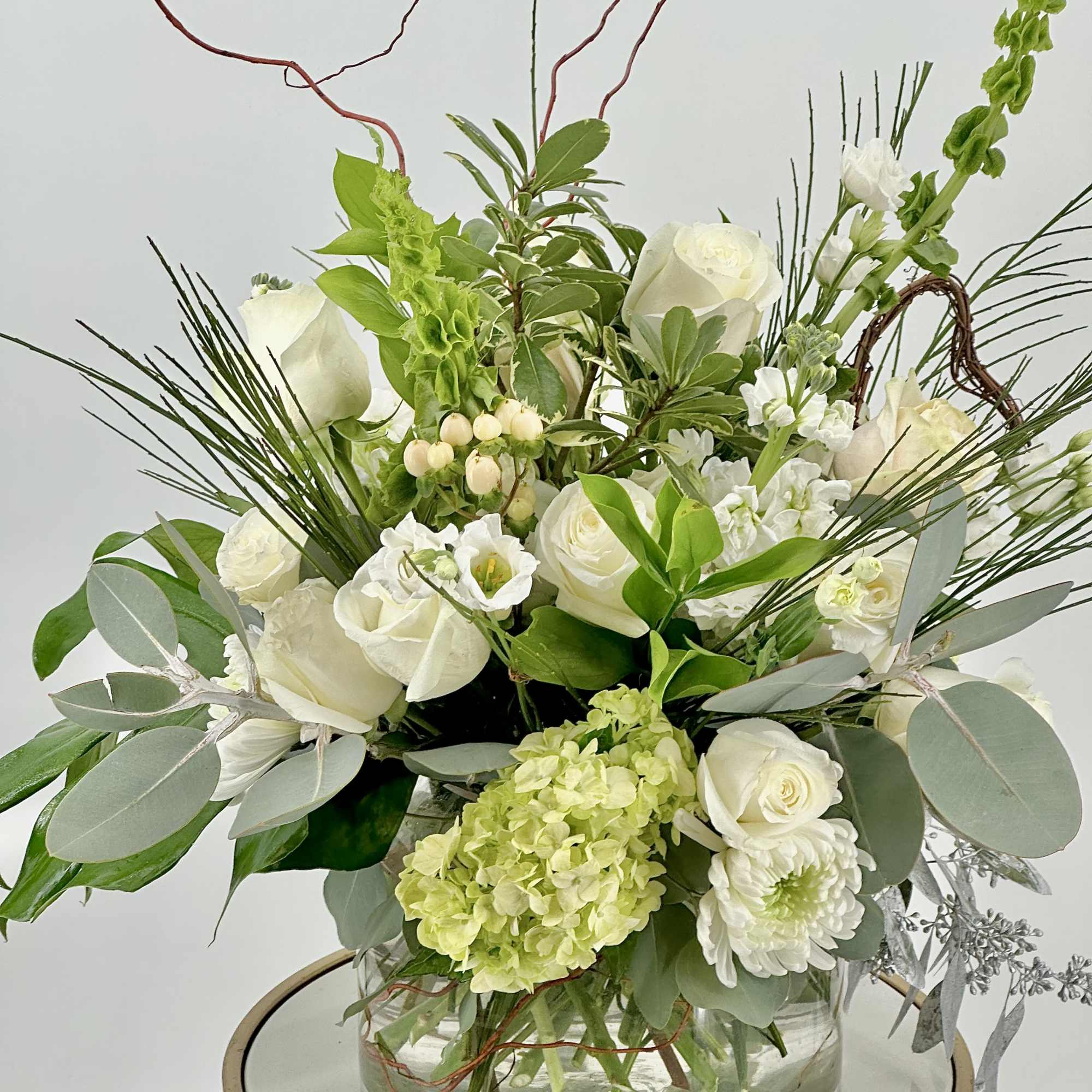 White roses and green hydrangea in a glass vase with mixed greenery
