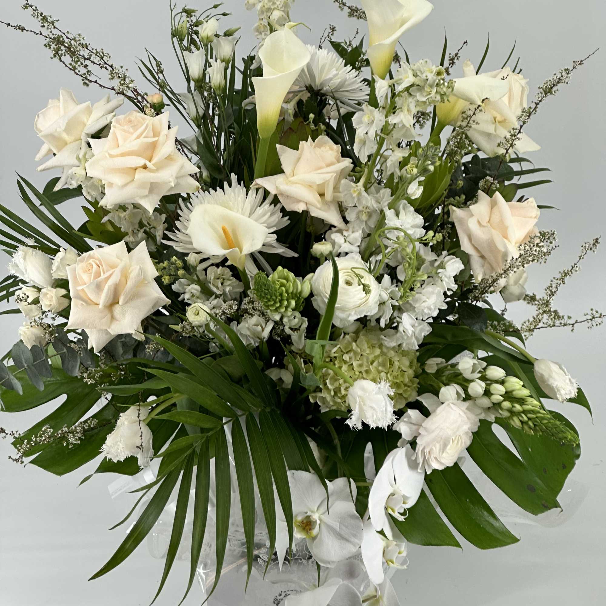 White floral arrangement with roses, calla lilies, and orchids in a clear vase