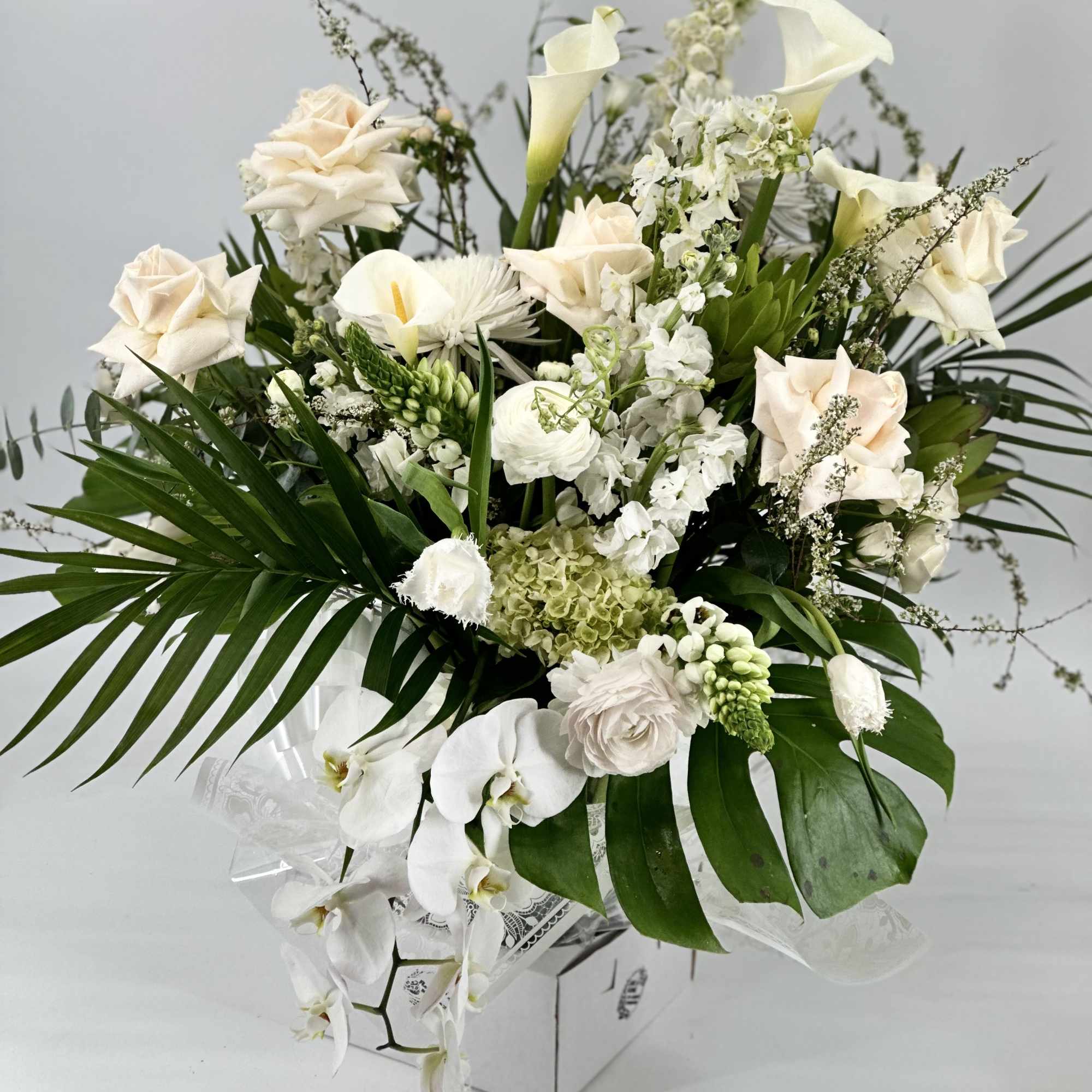 White floral arrangement with calla lilies, roses, and orchids in a box