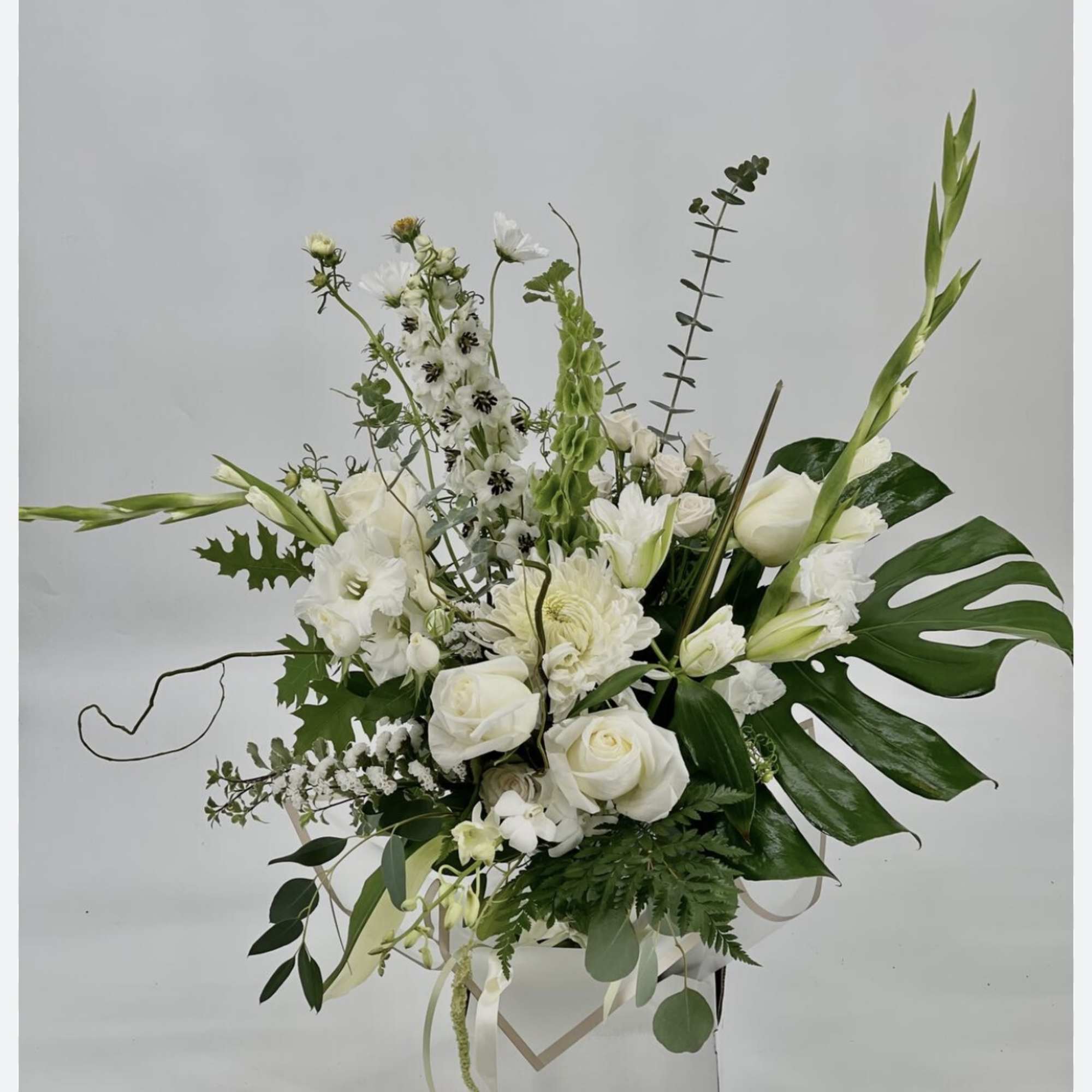 White floral arrangement in a white box with tall greenery and roses