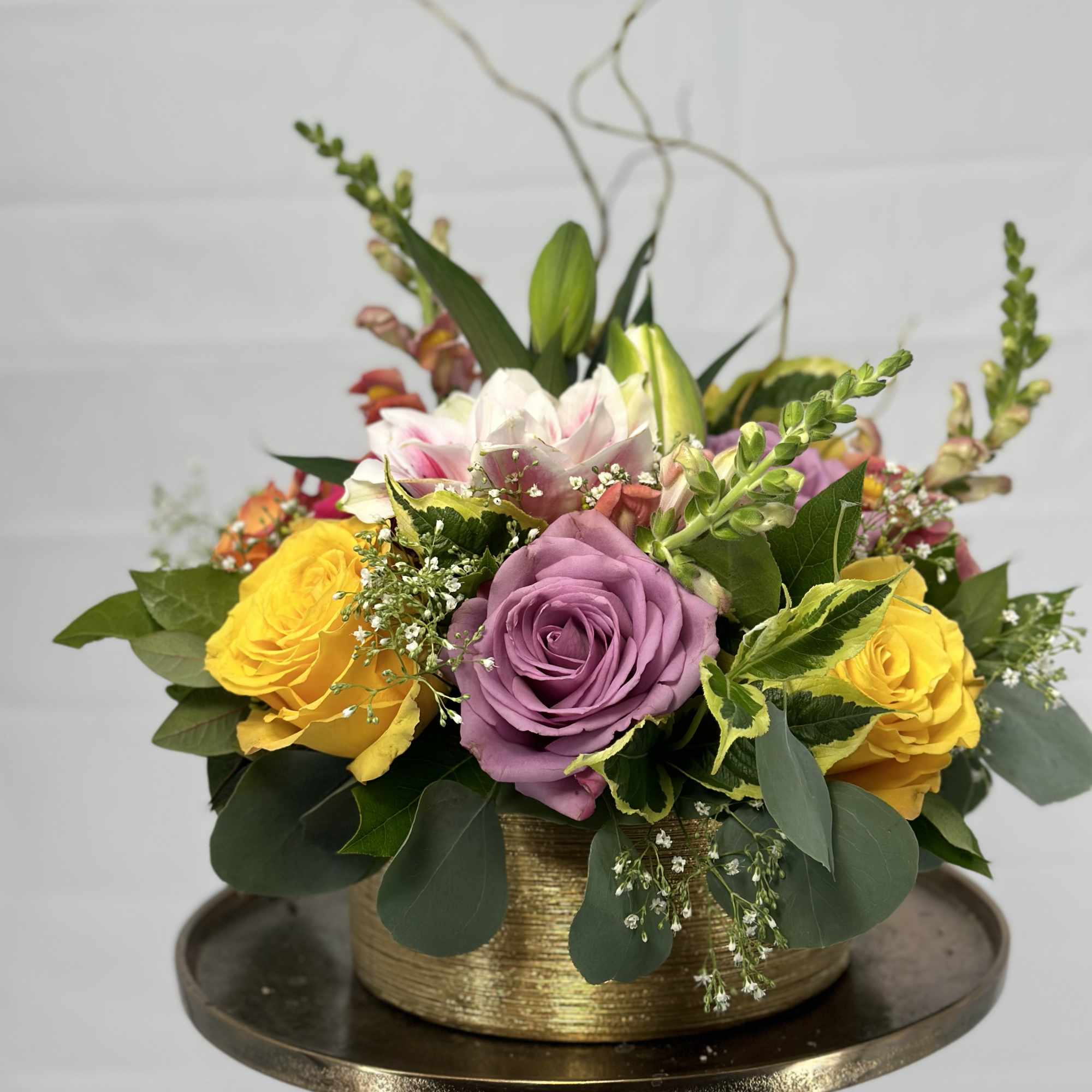Mixed rose arrangement in a gold container with purple and yellow blooms