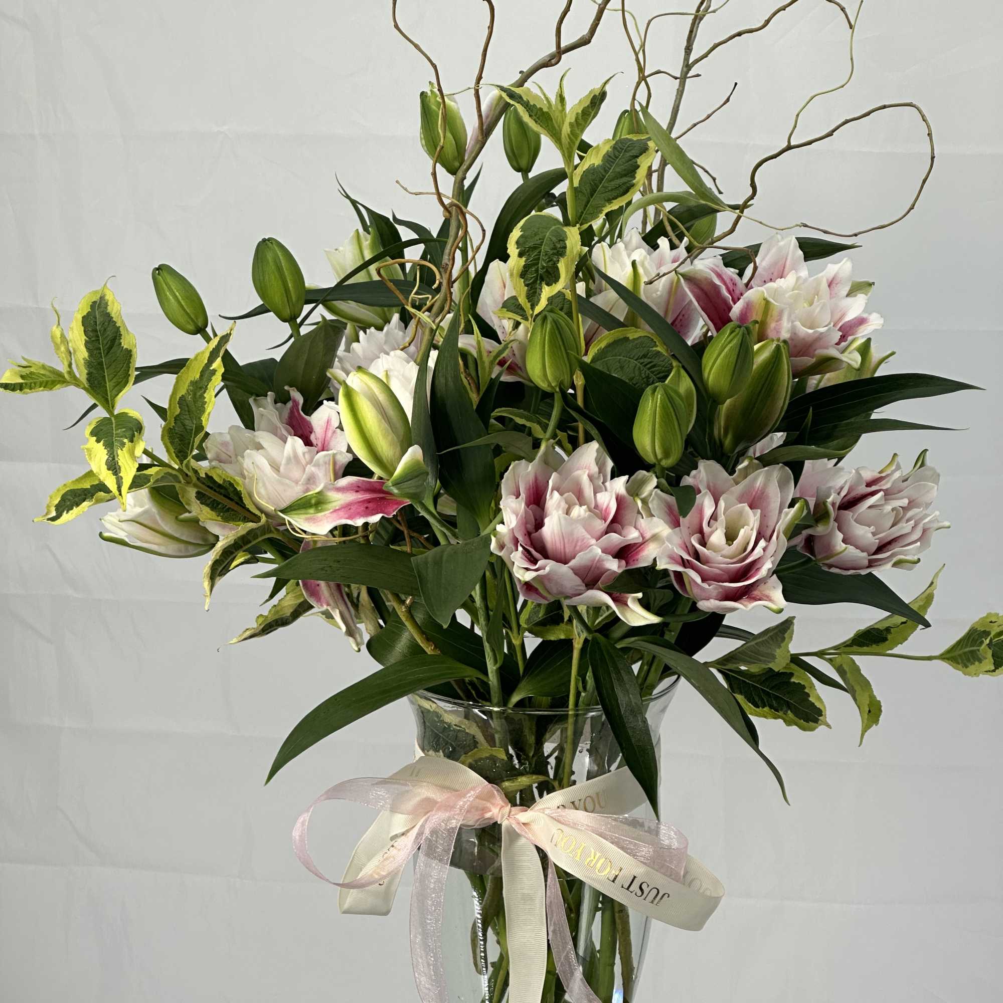 Pink and white lilies in a glass vase with a ribbon
