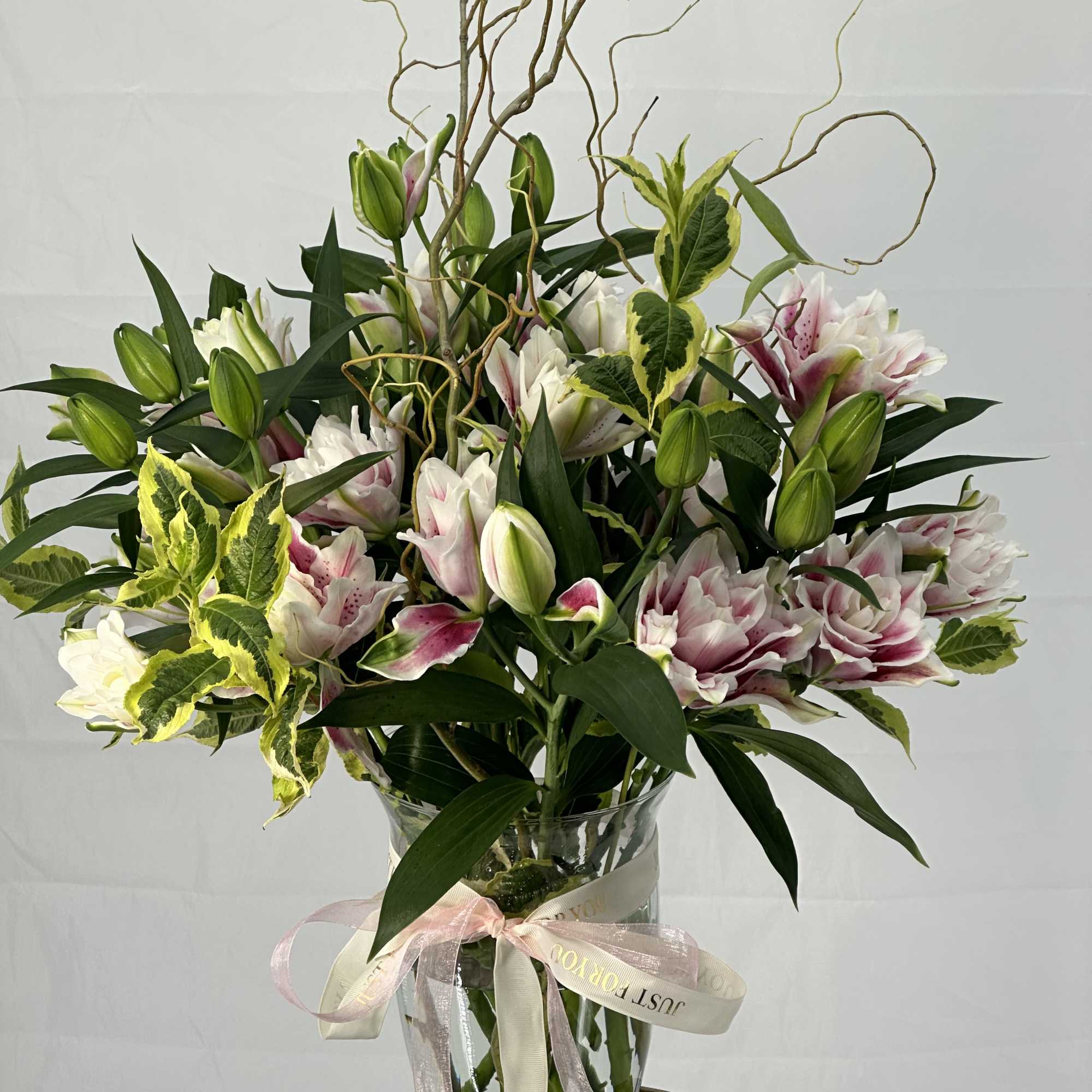 Pink and white lilies in a clear glass vase with a ribbon