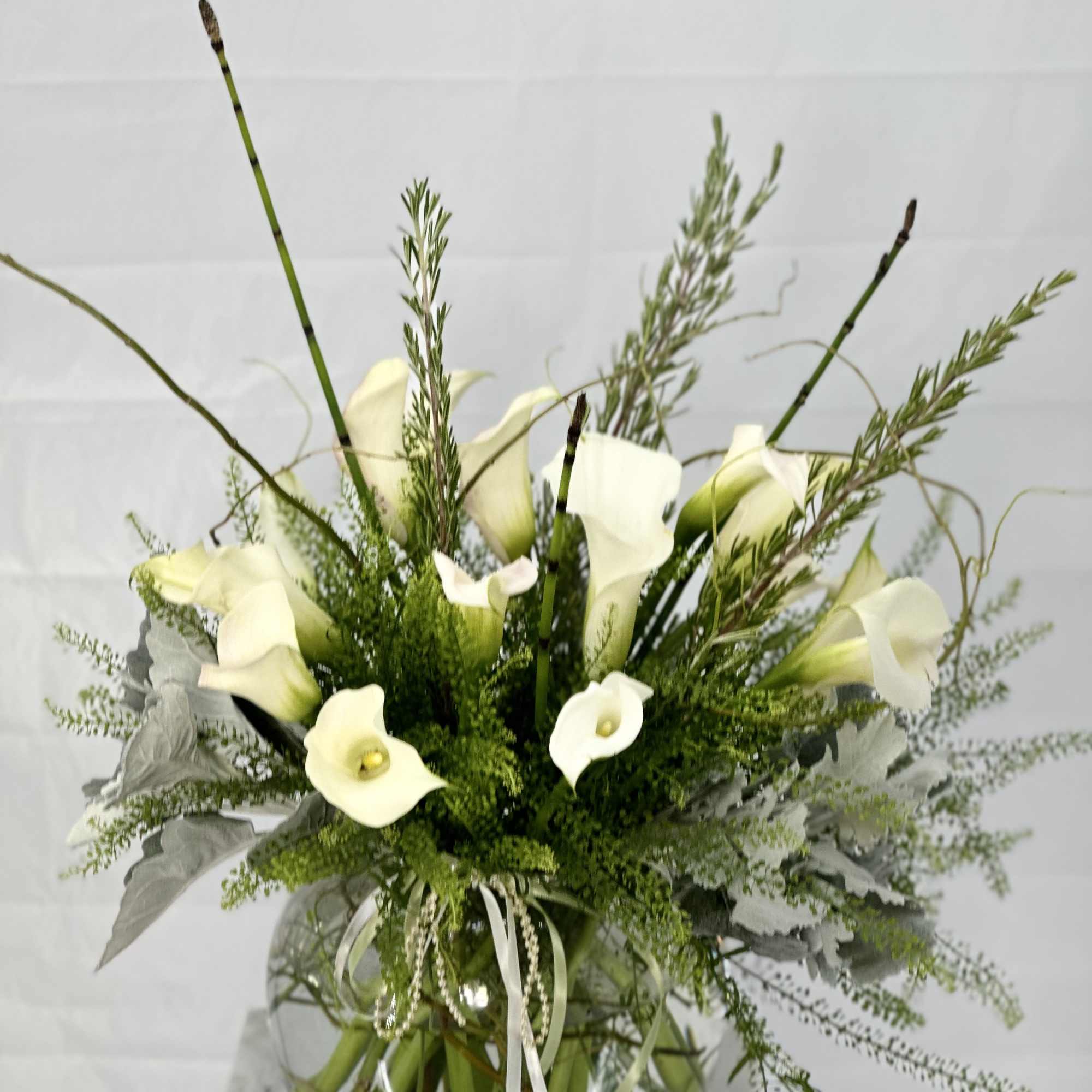 White calla lily arrangement in a glass vase with greenery
