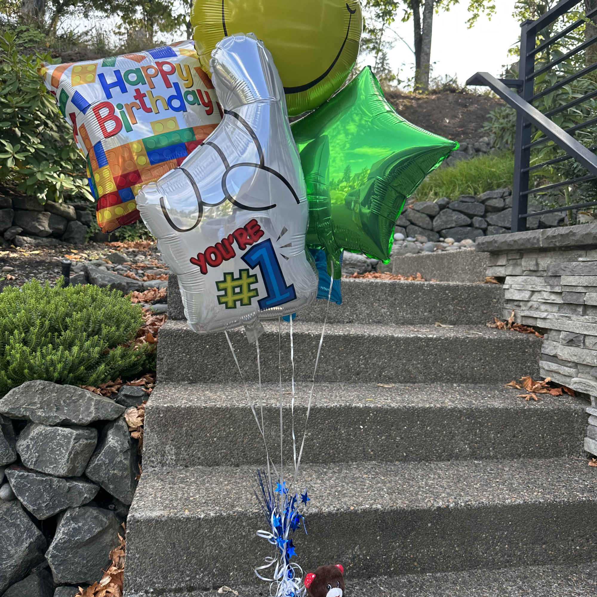 Birthday balloons with a teddy bear on outdoor steps