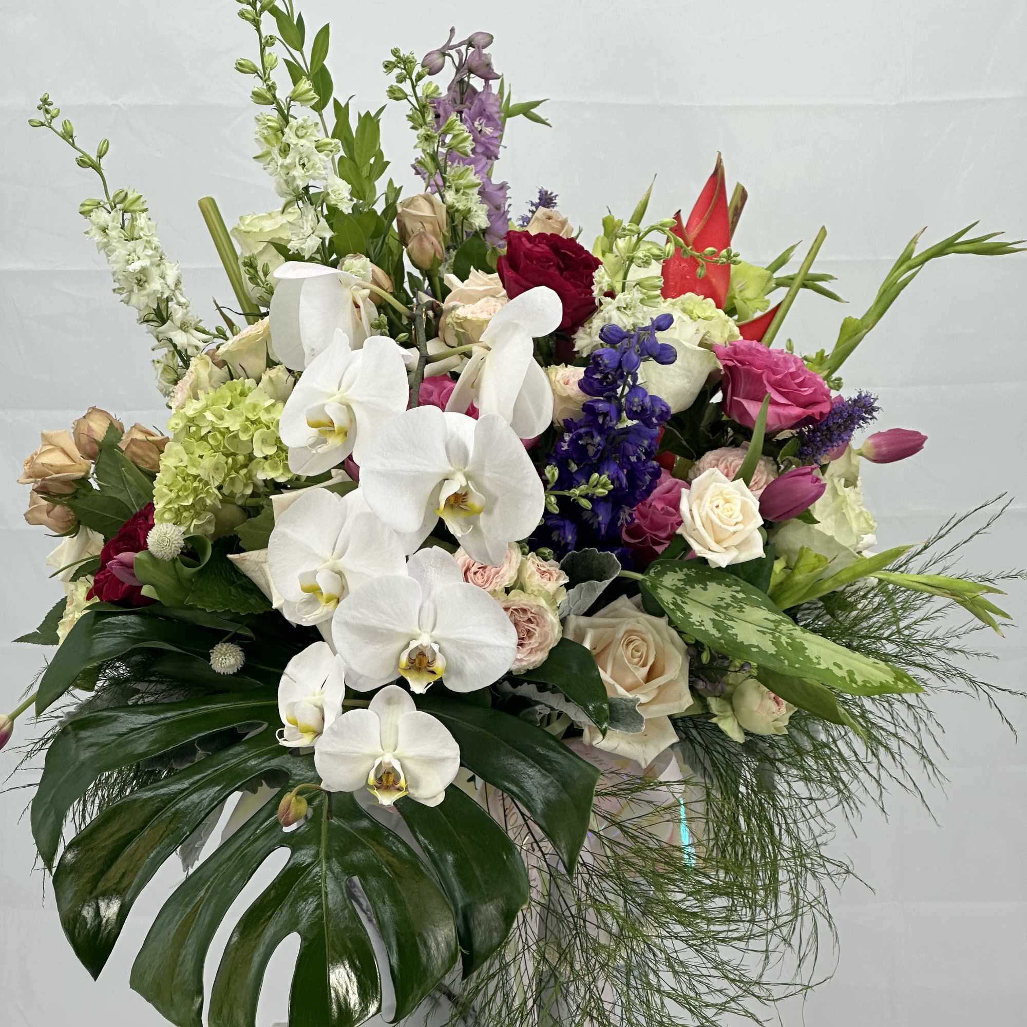 Mixed bouquet with white orchids, roses, and purple flowers in a white container