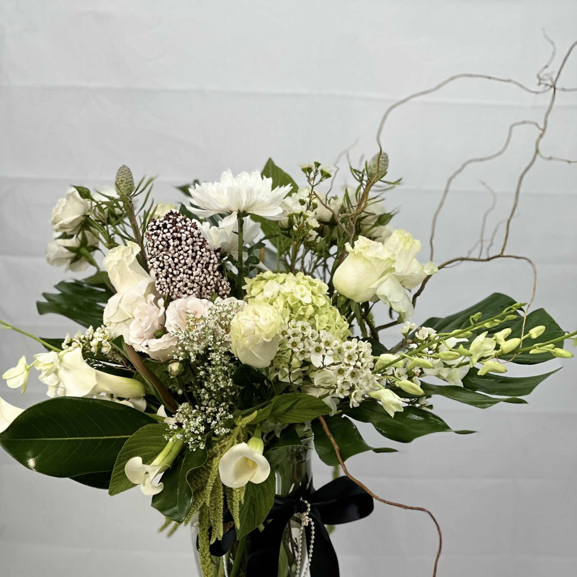 White floral arrangement in a glass vase with a black ribbon
