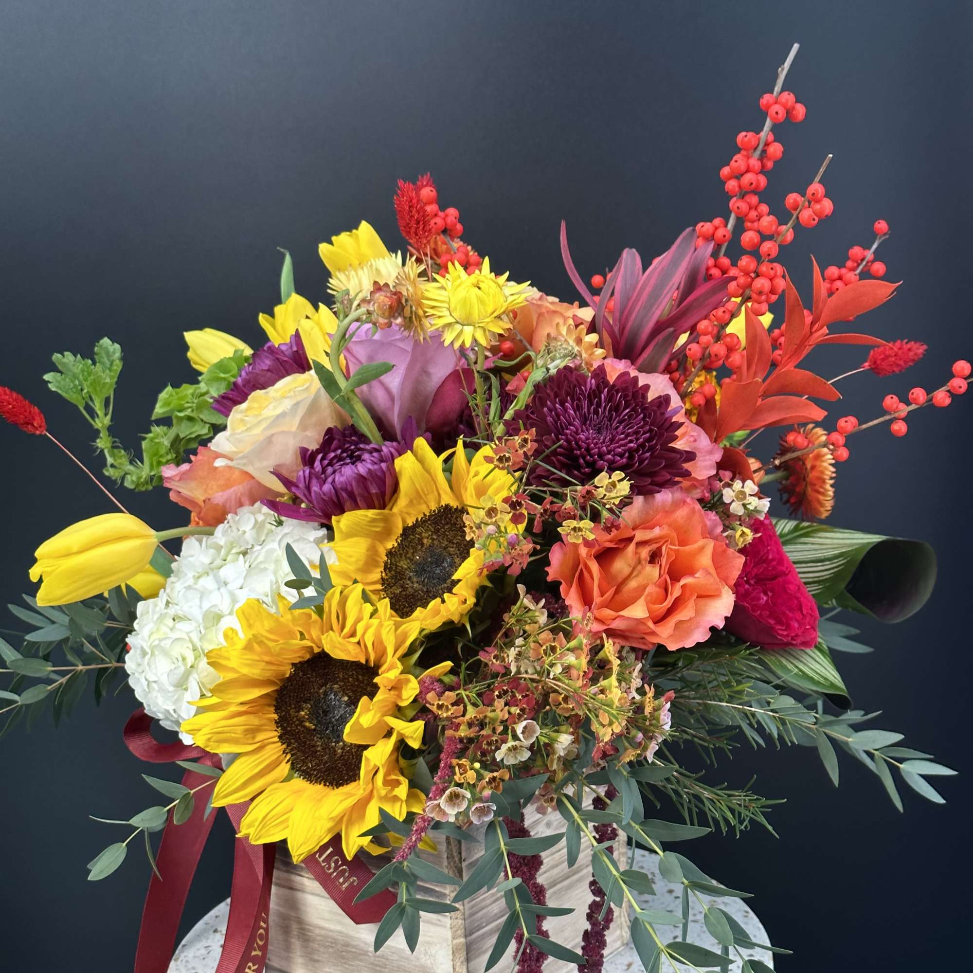 Bright mixed bouquet with sunflowers, roses, and berries in a wooden box